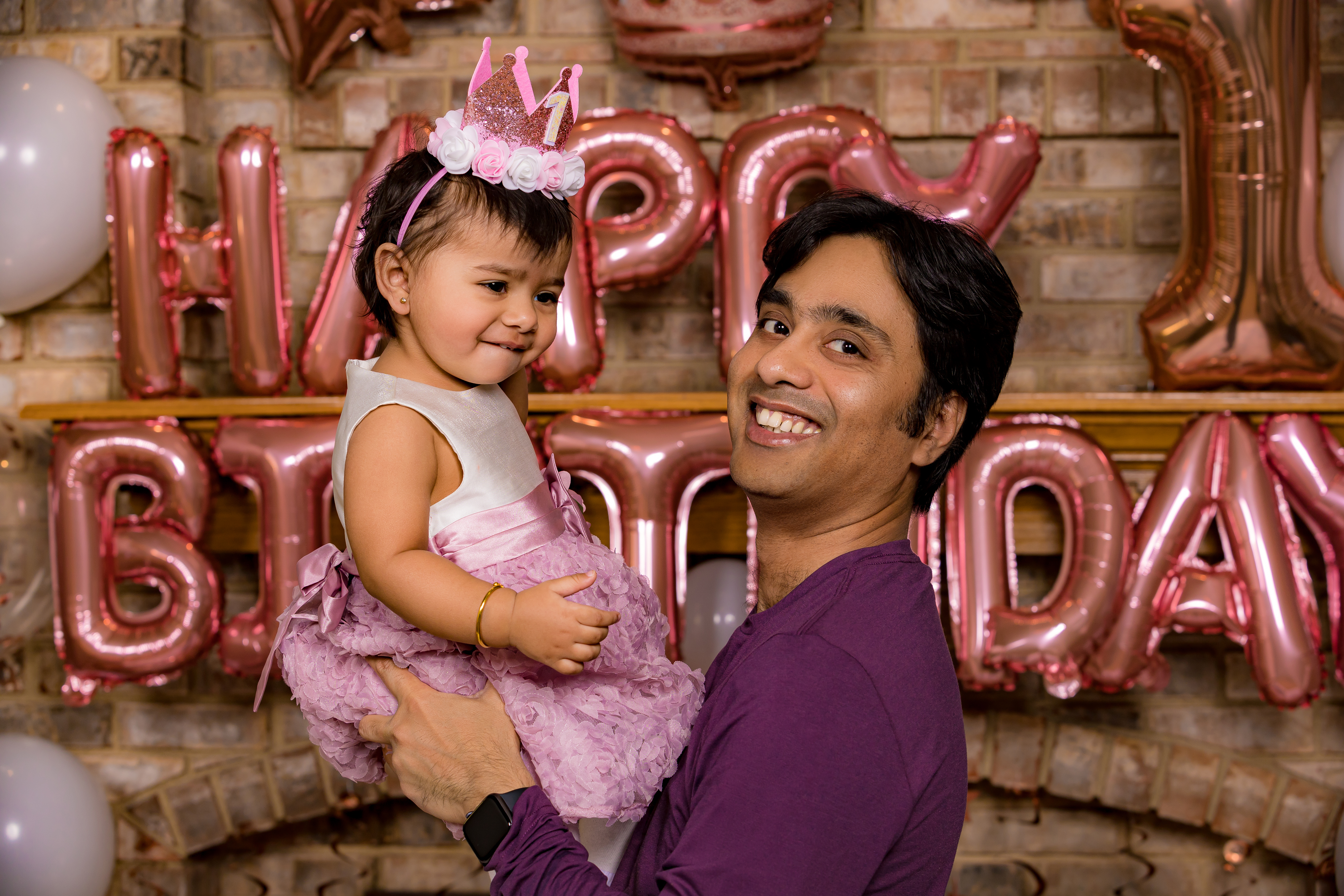 Dad holding baby girl both smiling at camera in front of birthday balloons — IDTPhoto cake smash
