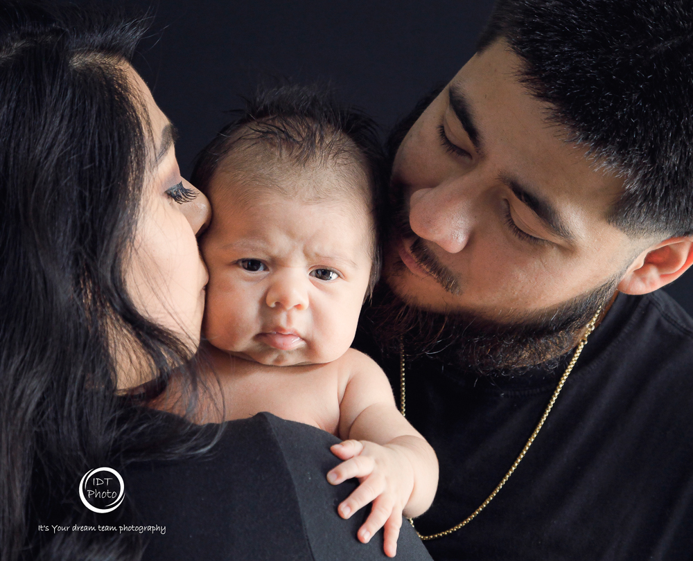 Both parents kissing baby's cheeks while baby makes an adorably grumpy face — IDTPhoto 3-month milestone