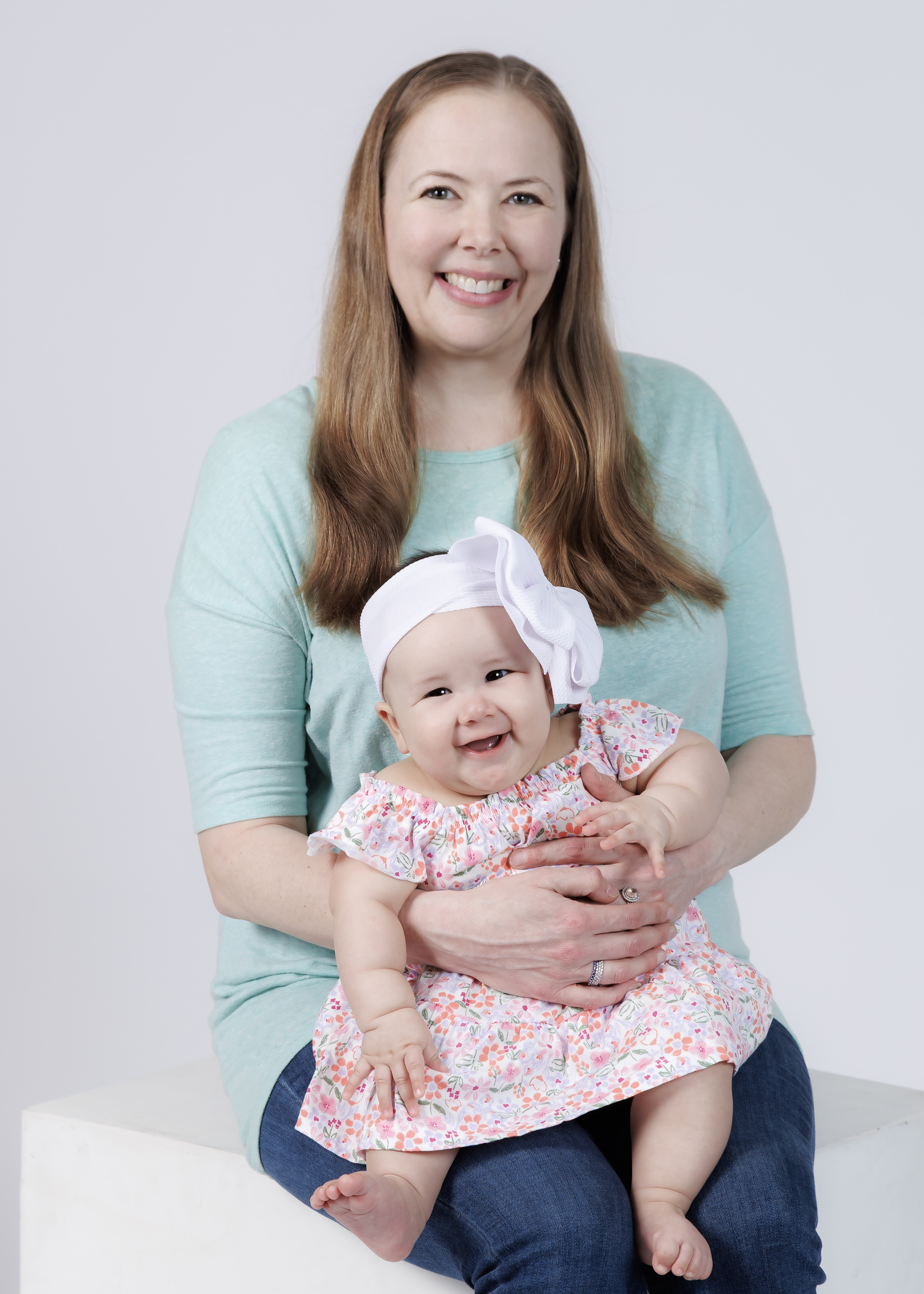 Mom holding smiling 6-month baby girl in floral dress with white bow headband — IDTPhoto milestone session