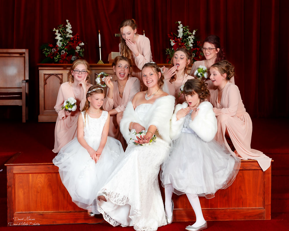 Bride surrounded by bridesmaids and flower girls all laughing and making silly faces at church altar — IDTPhoto wedding