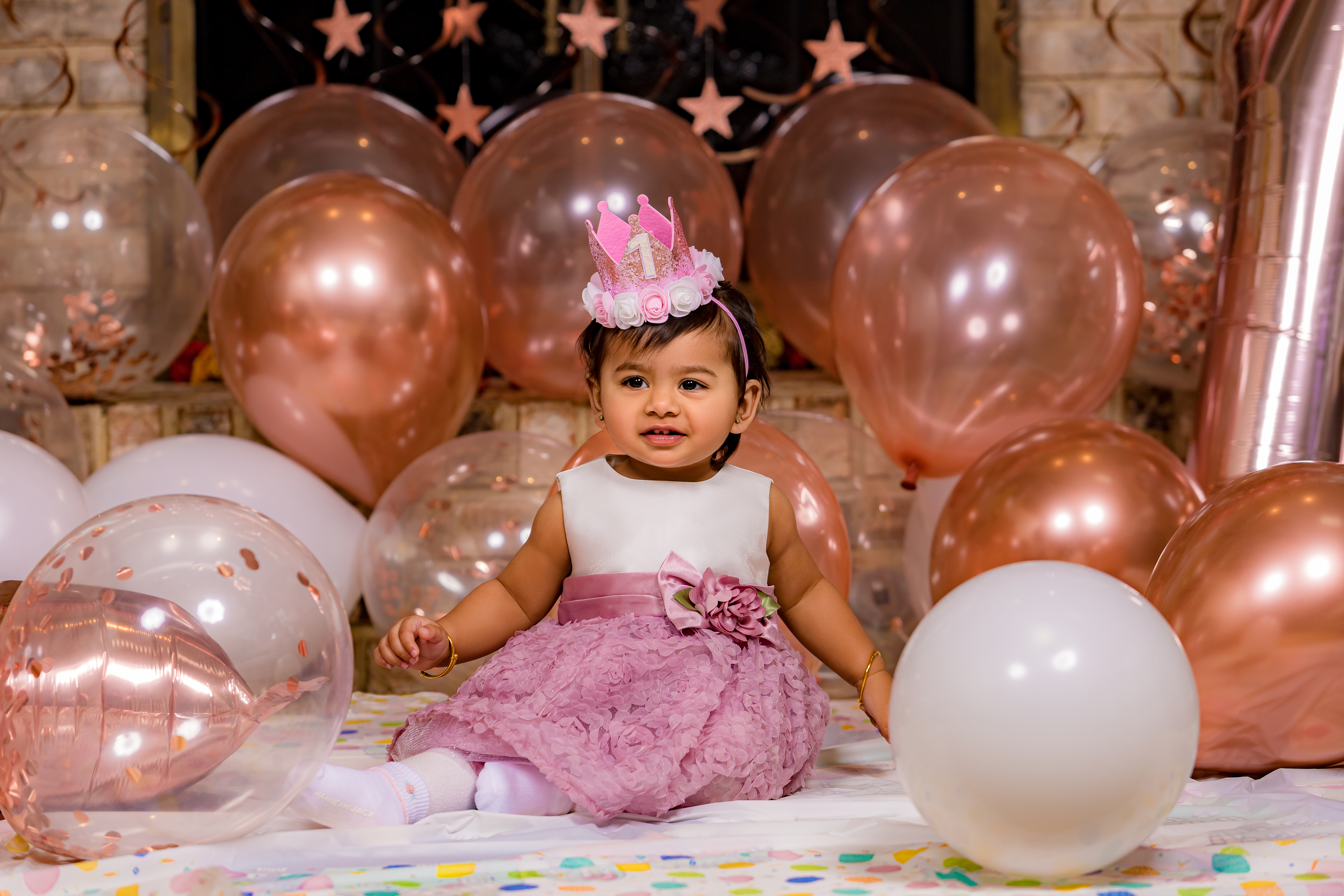 Baby girl in pink birthday dress with crown among rose gold and white balloons — IDTPhoto studio cake smash