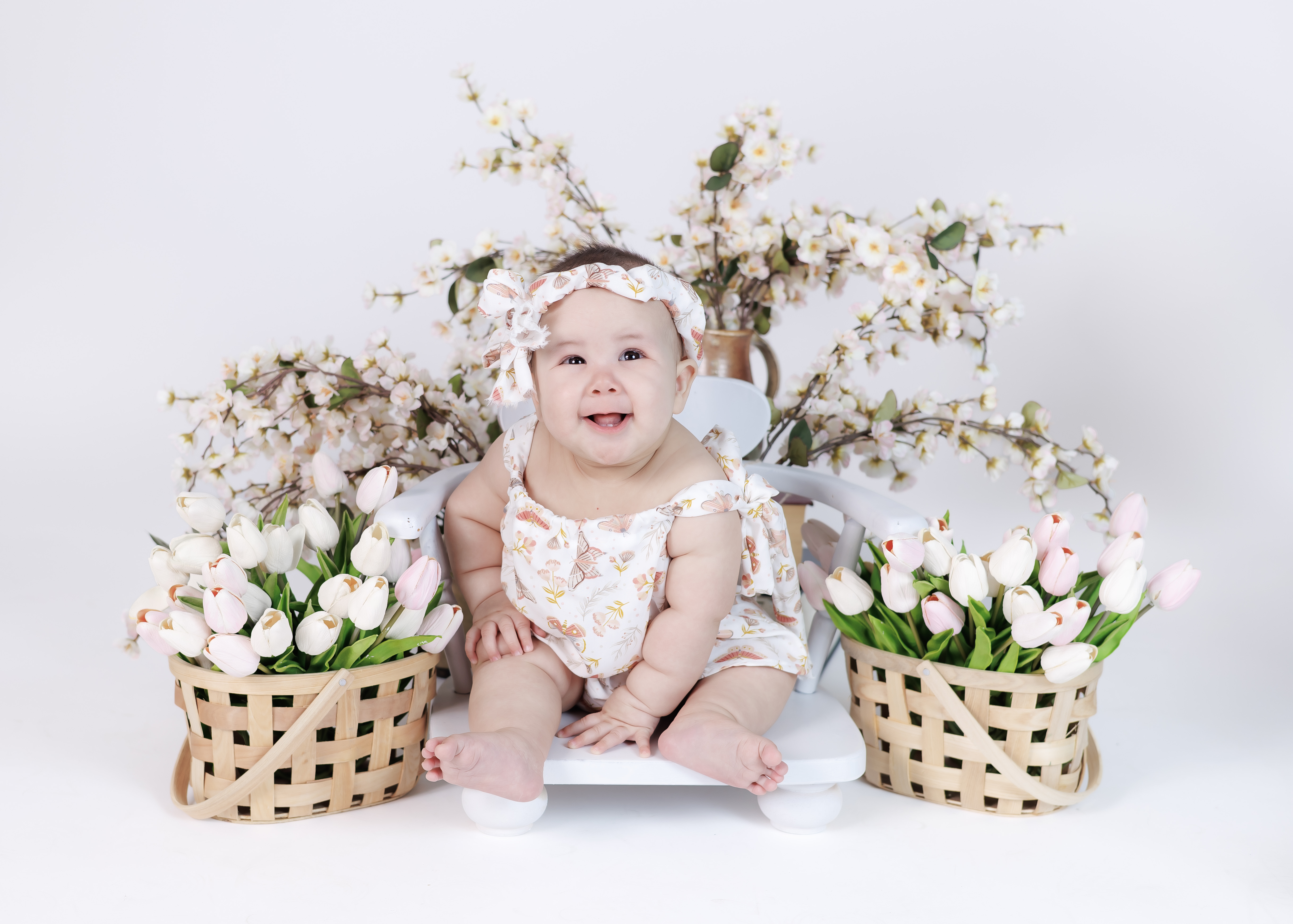 6-month baby girl in butterfly romper with bow headband among tulip basket arrangements — IDTPhoto Aurora IL
