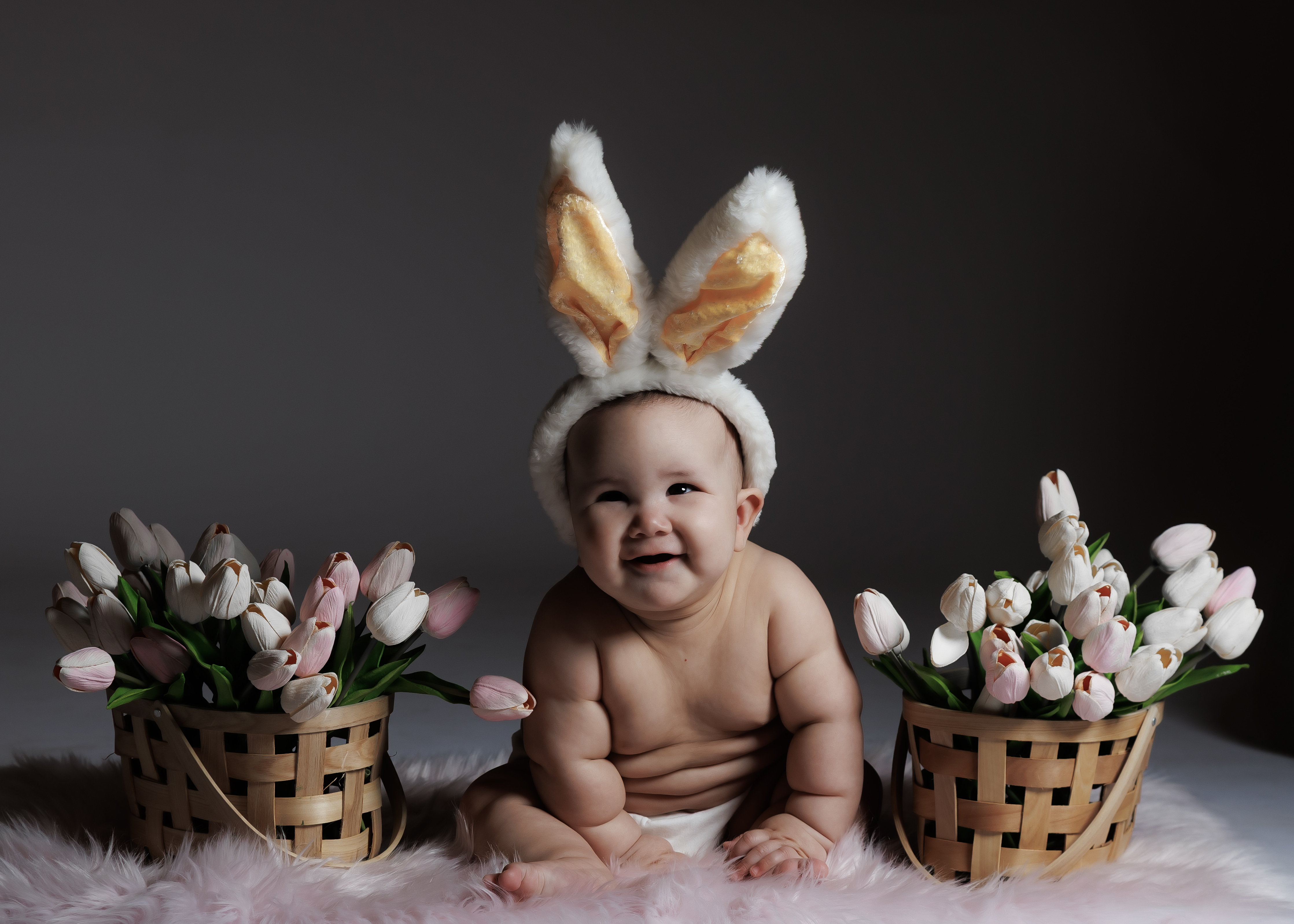 6-month baby with bunny ear headband laughing big between pink and white tulip baskets — IDTPhoto studio sitter session