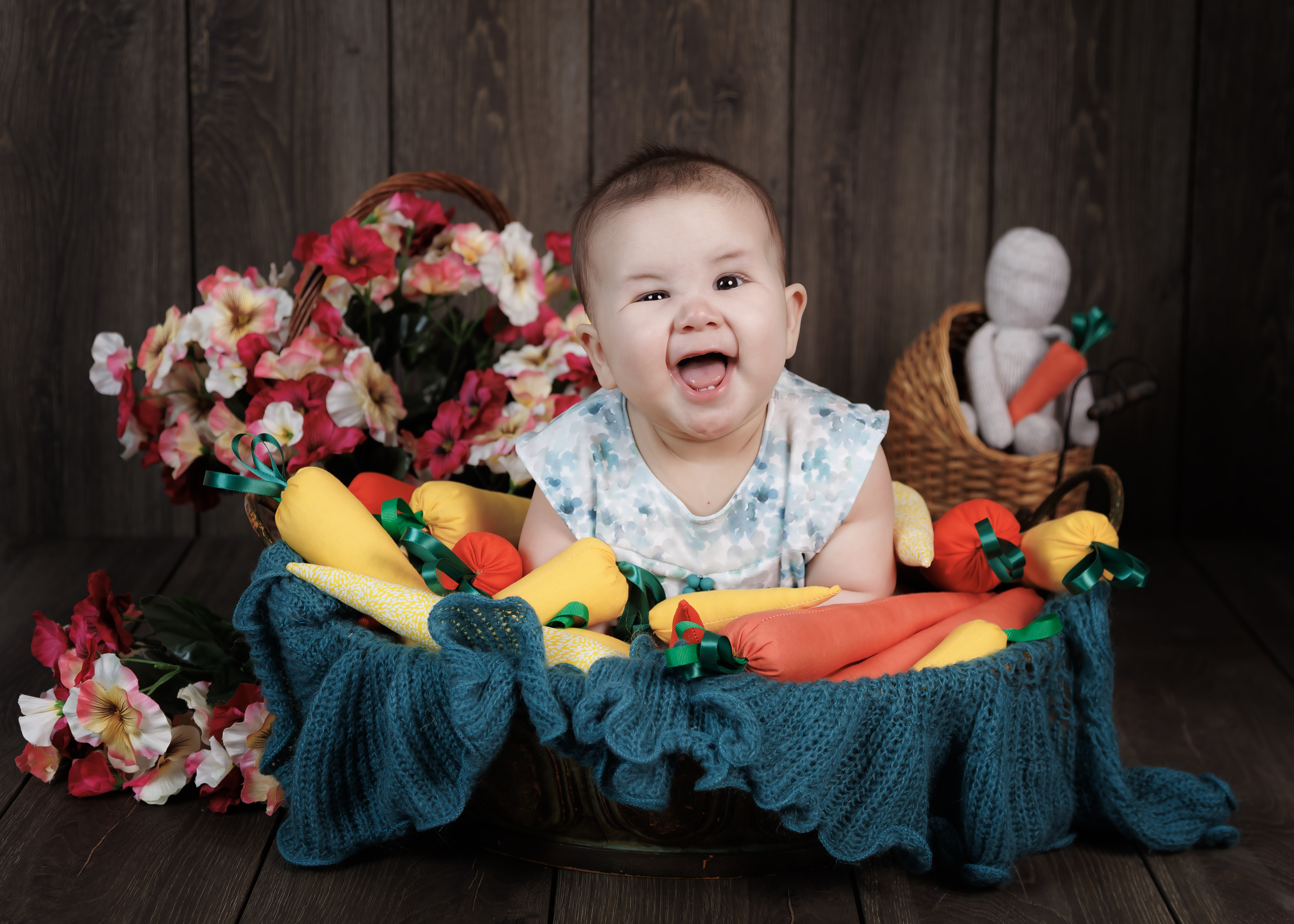 Baby laughing in wicker basket with fabric carrots and floral props — themed 6-month session by IDTPhoto