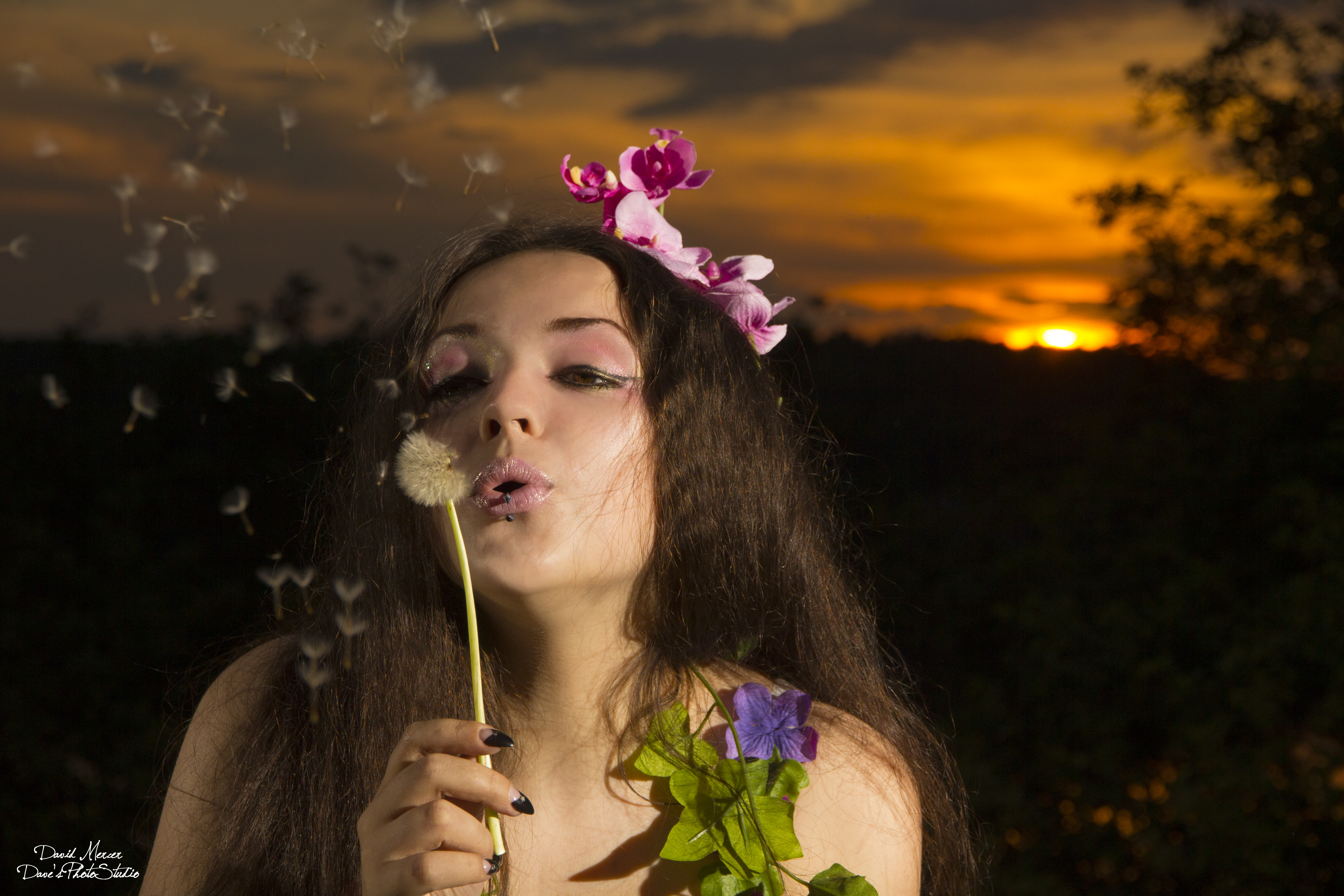 Artistic portrait — model blowing dandelion with orchid crown at golden sunset — IDT Photo
