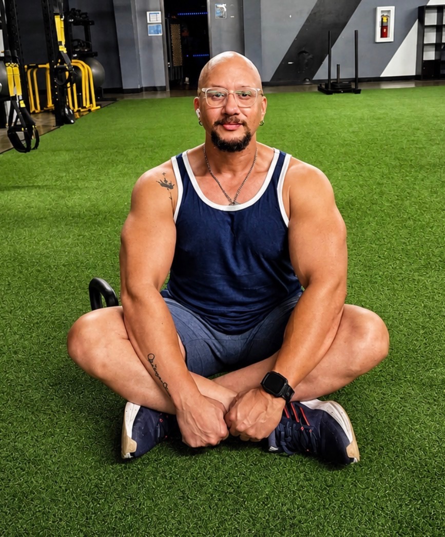 Coach Rey seated on gym turf — relaxed and confident