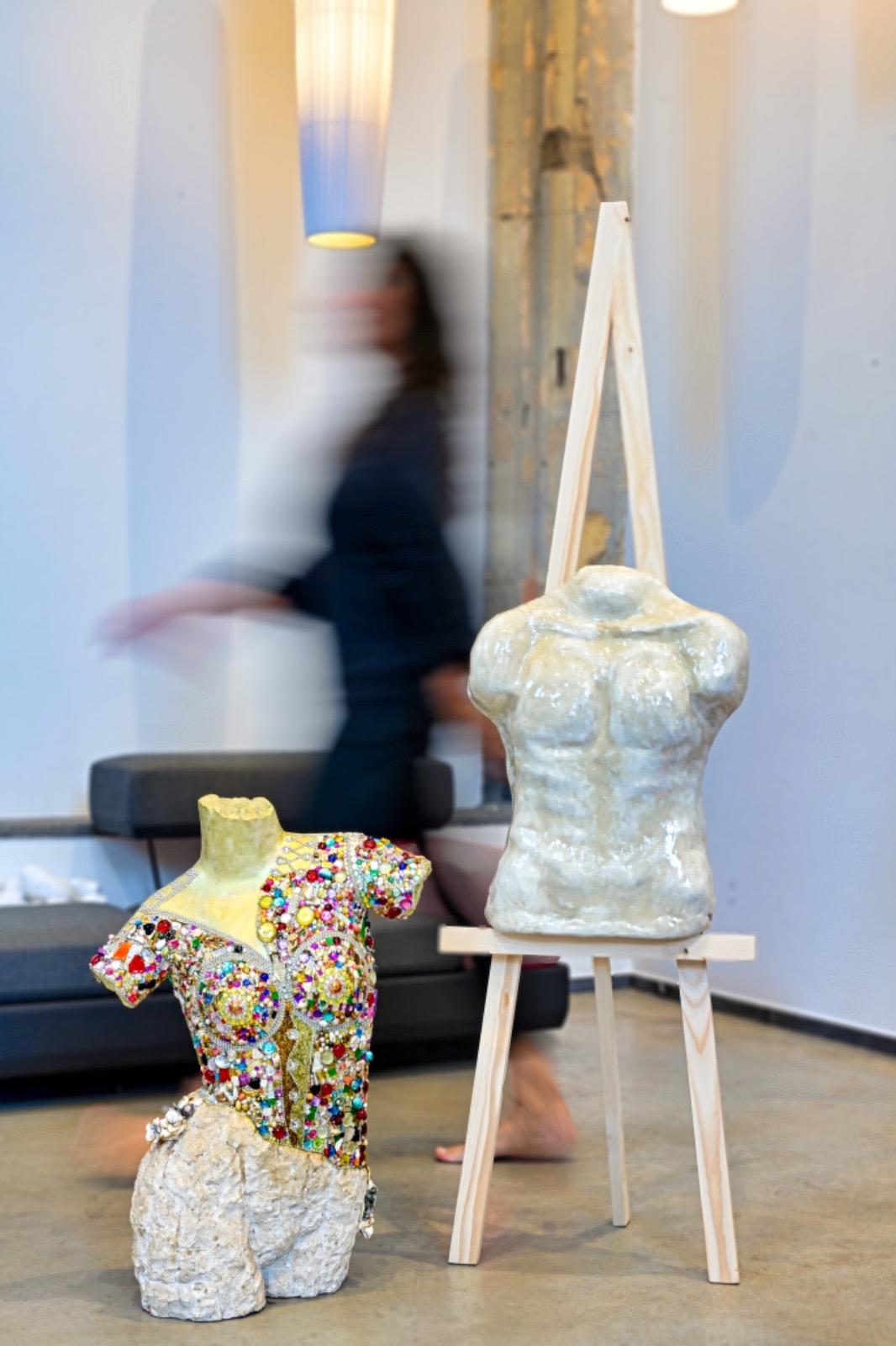 Two busts displayed on easels in gallery space with artist walking past