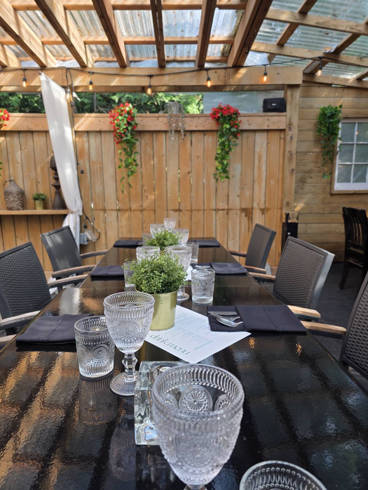 Olio patio table set for a private dinner with crystal glasses, dark napkins, and fresh greenery under a pergola