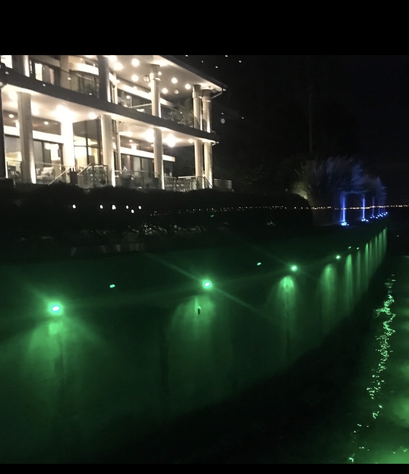 Culbreath Isles South Tampa waterfront estate at night — green underwater seawall lights glowing into canal, blue accent uplights on tropical landscape by LED Artistry