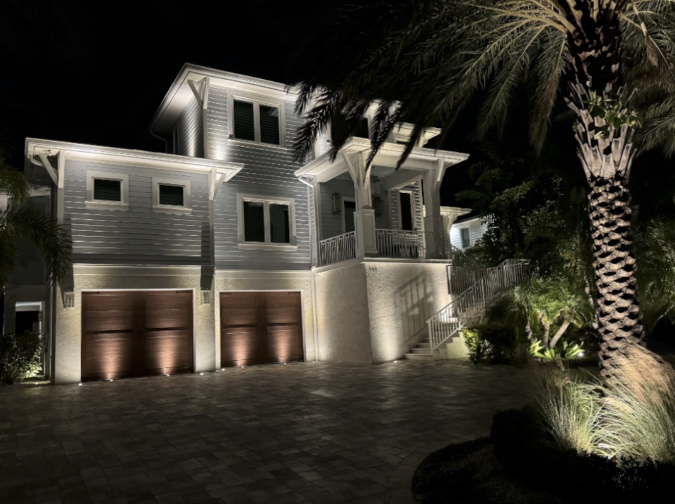 Coastal home with 3-car garage and architectural LED uplighting with paver driveway at night