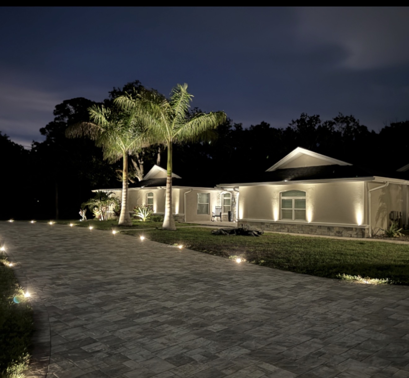 Home with stunning paver driveway LED lighting and illuminated palm trees
