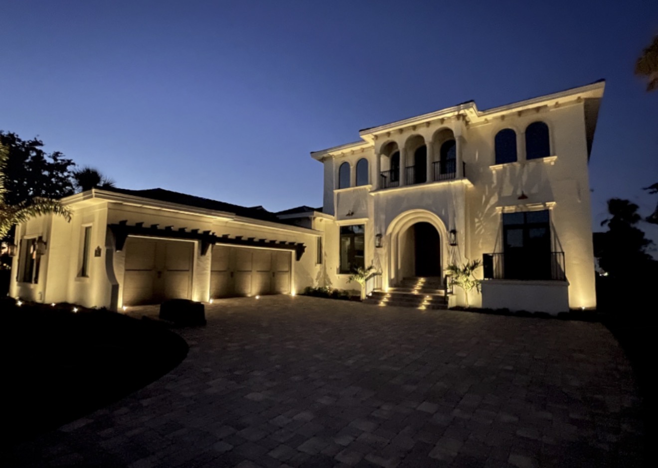 Large luxury home with paver driveway and full architectural LED uplighting at night