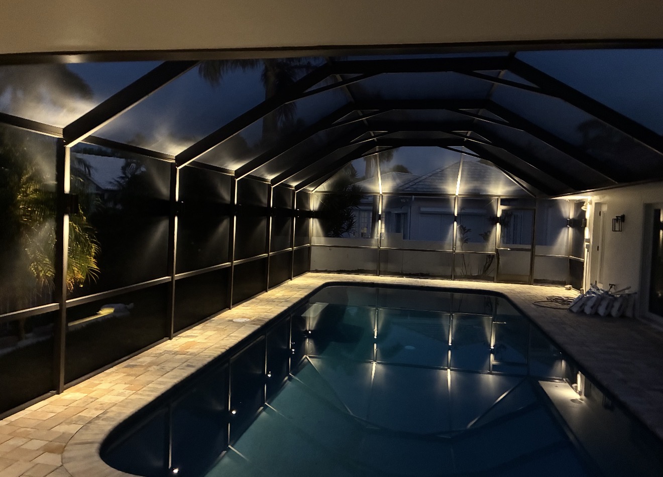 Pool cage with warm white architectural LED lighting on every beam at night, pool reflection