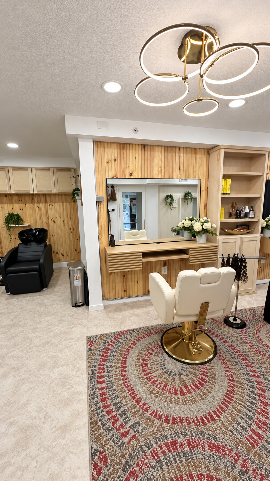 Spacious salon suite with cream styling chair, natural wood paneling, built-in cabinetry, shampoo bowl, and modern gold ring chandelier at Posh Salon Suites in Spring TX