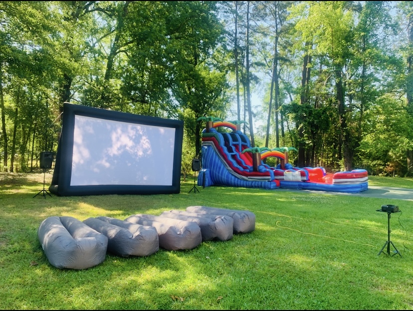 Outdoor movie night setup with 24ft screen, bean bag seating, speakers, and Baja Splash water slide in background