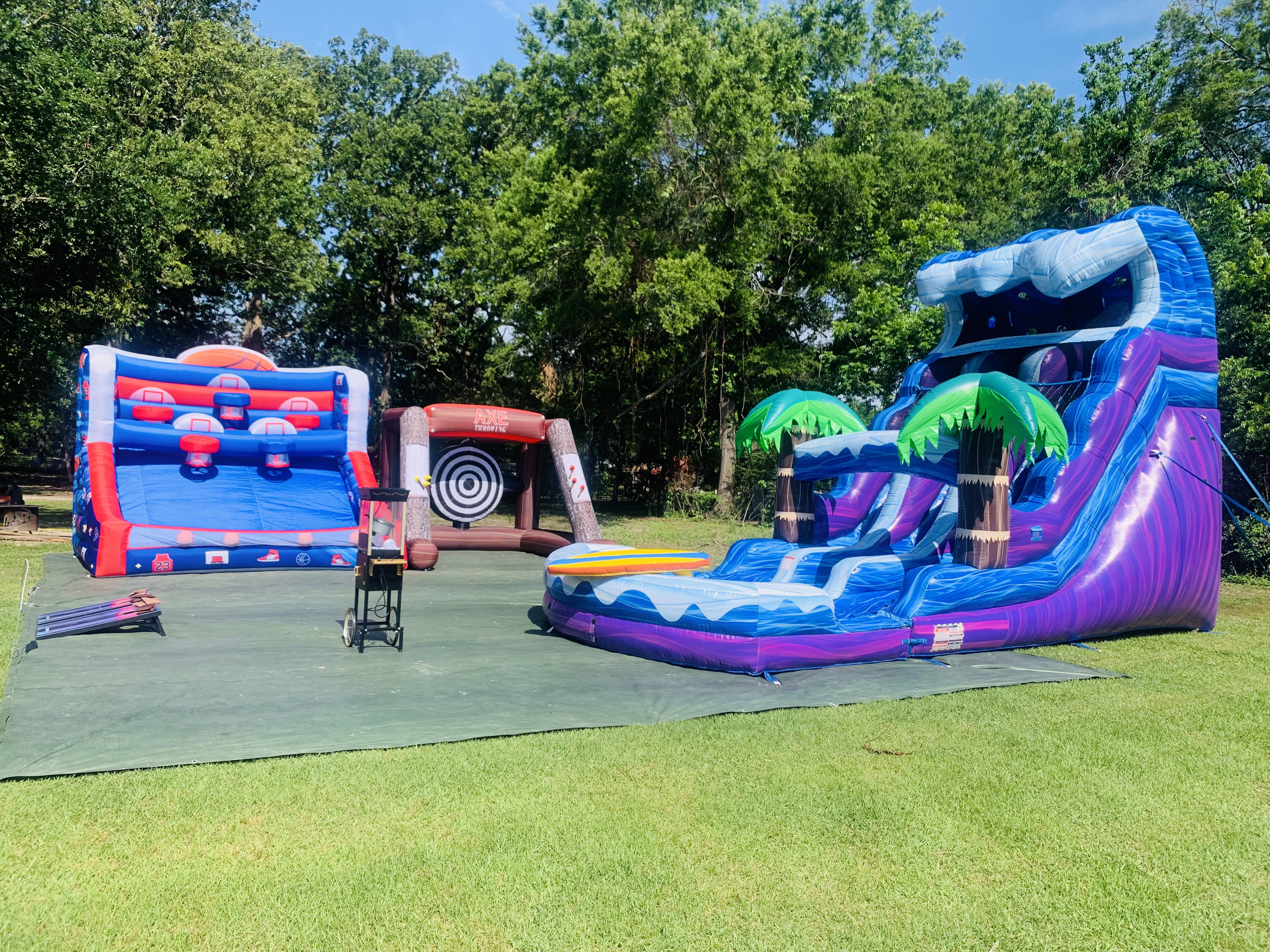 Basketball shootout, Bullseye Blast axe throwing, and Palm Tree Plunge water slide setup on green grass