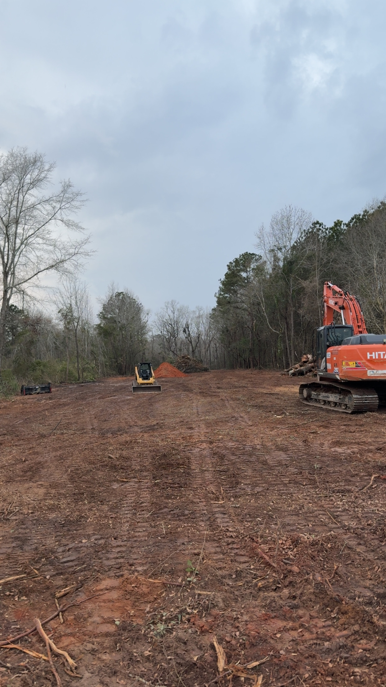 Land clearing and grading project with Hitachi excavator and skid steer working red clay soil on a large rural lot, by Stukes Construction