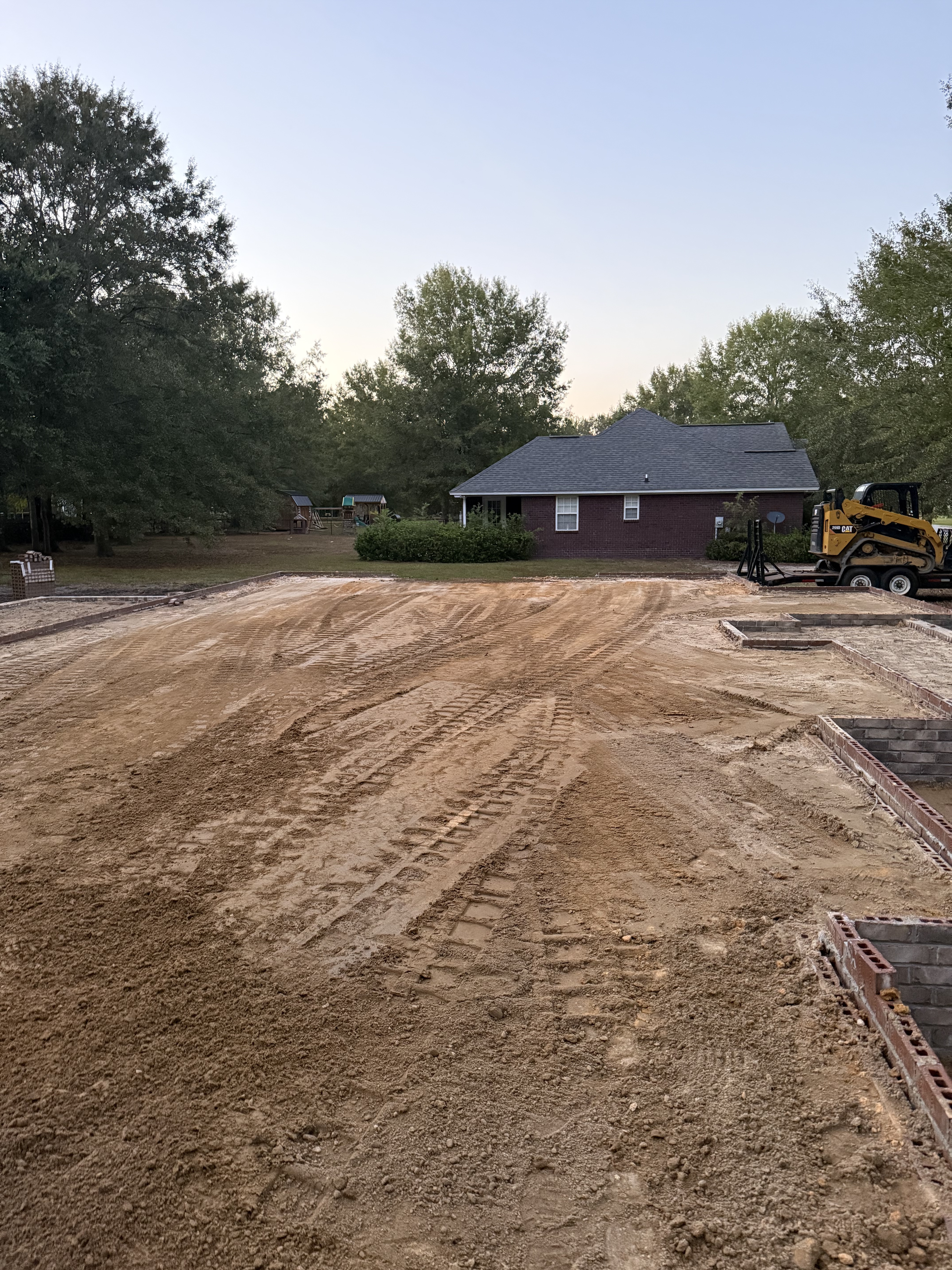 Precision grading for residential foundation with CAT skid steer on compacted soil next to brick home, by Stukes Construction