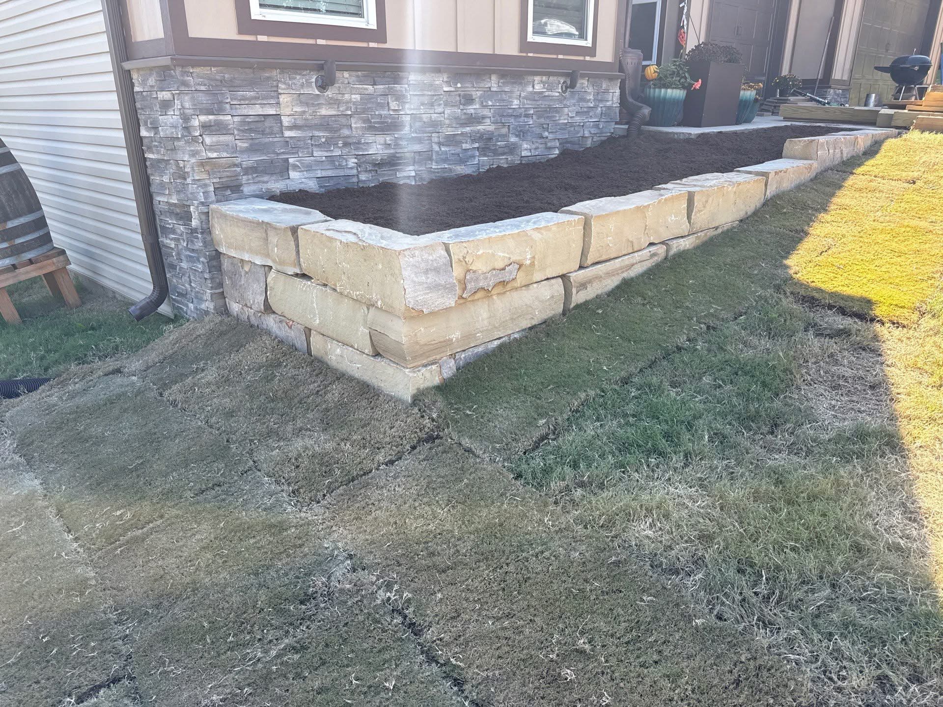 Completed stone veneer retaining wall with natural stone cap blocks on a residential property, built by Stukes Construction
