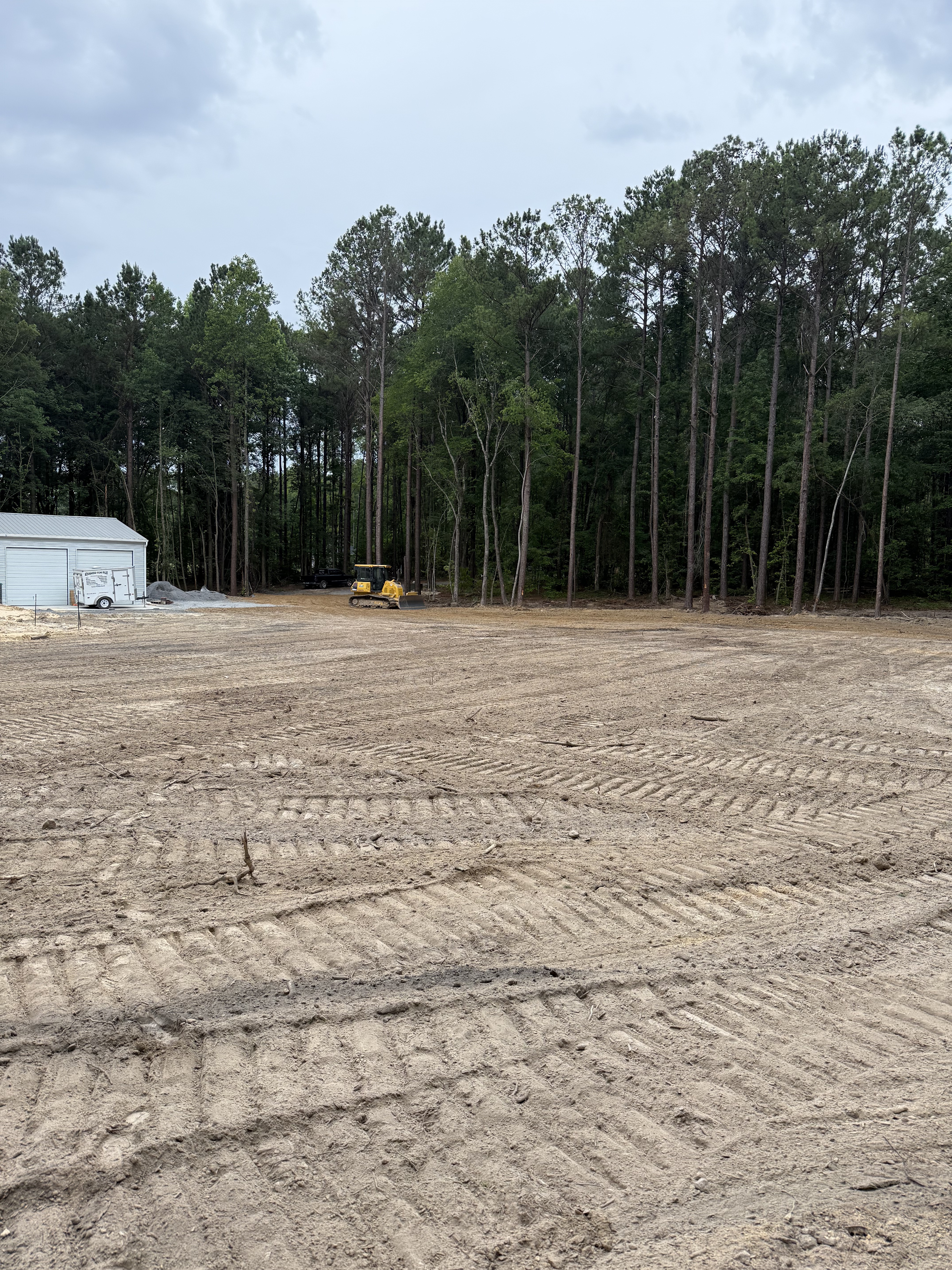 Graded residential lot with bulldozer and equipment on site, freshly leveled sandy soil with tree line in background, by Stukes Construction