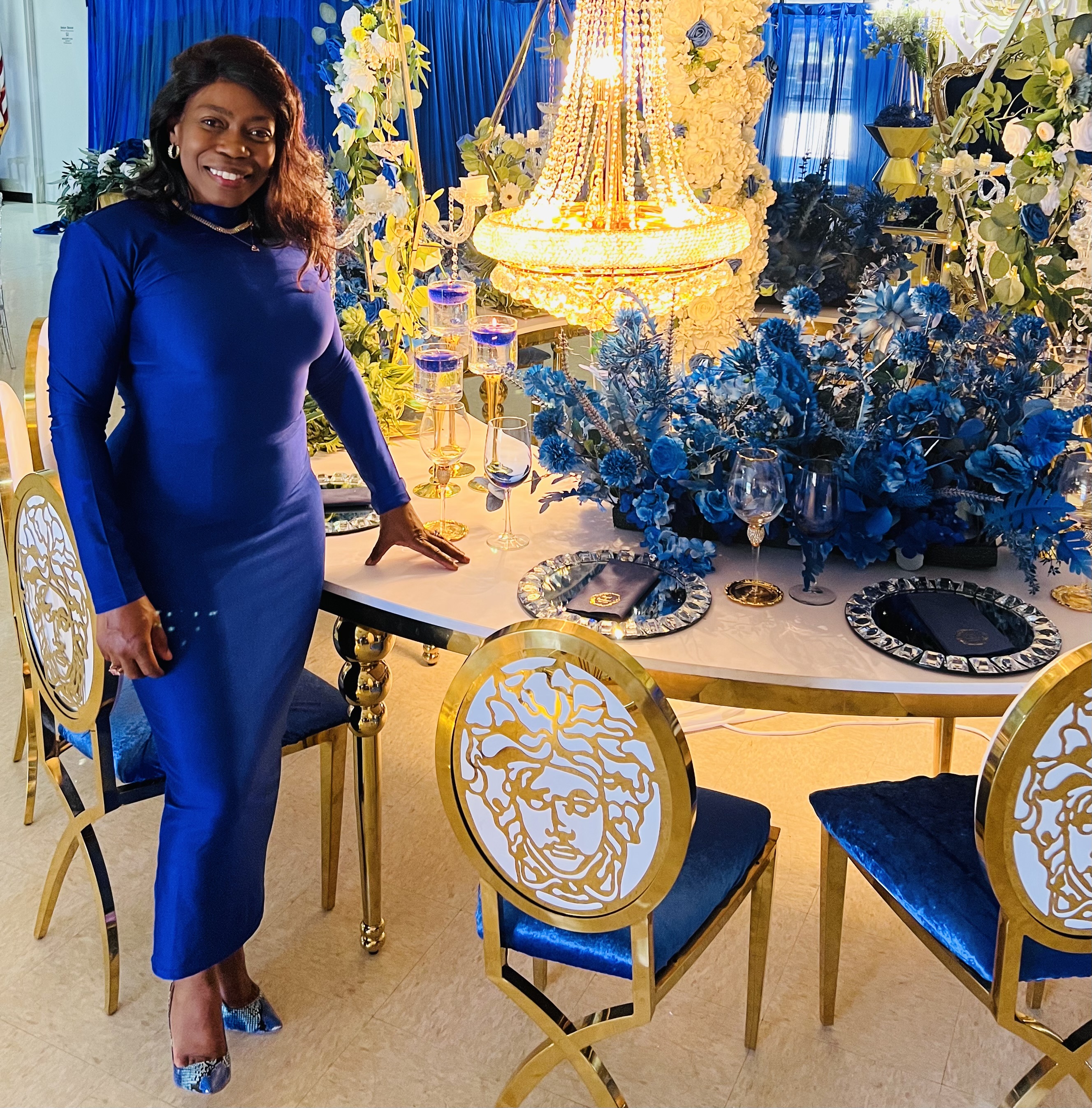 Dianne posing beside a royal blue and gold luxury table setup with chandelier and blue florals