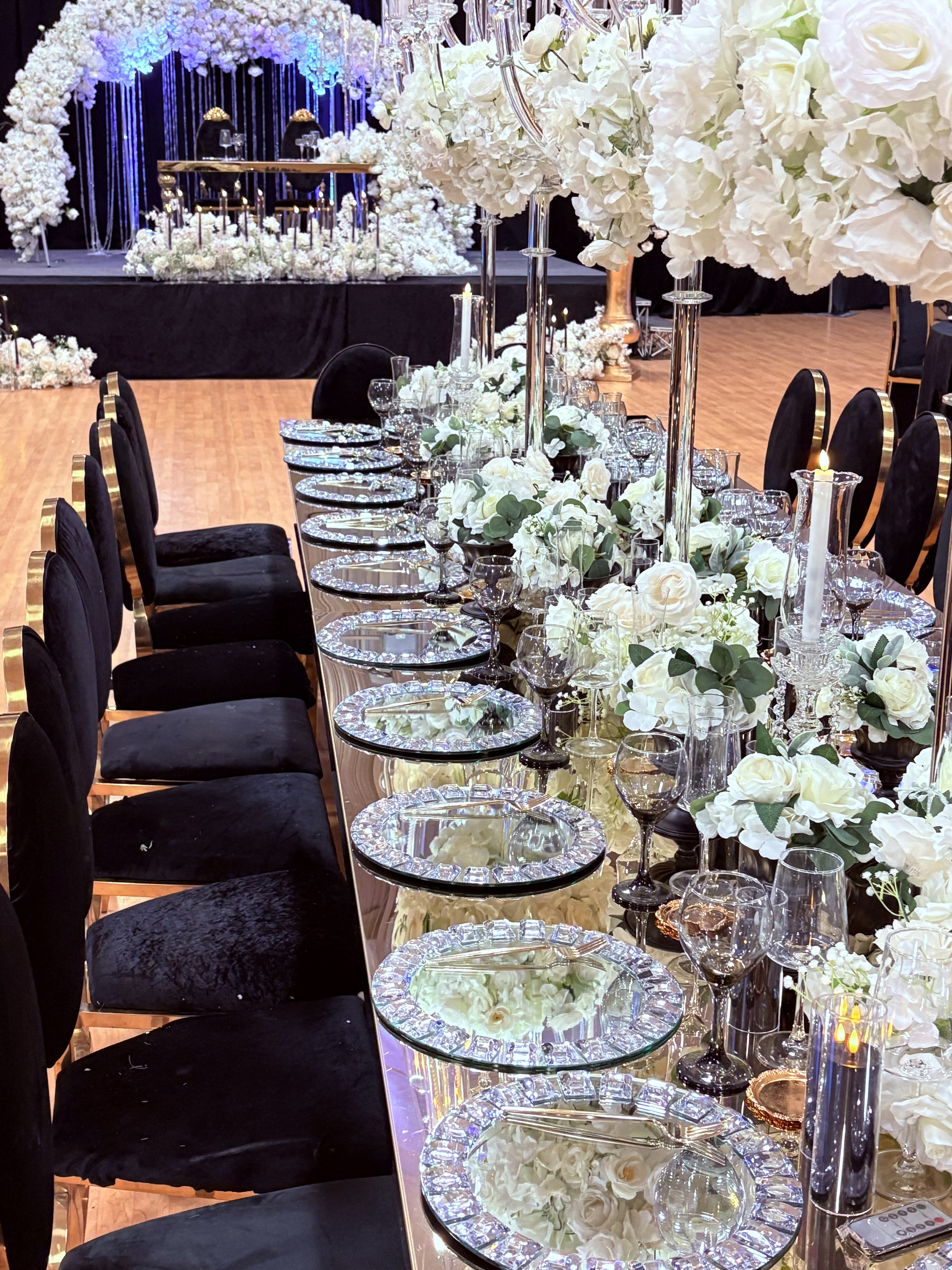Luxury mirror table with crystal charger plates, white rose floral runners, and black velvet chairs