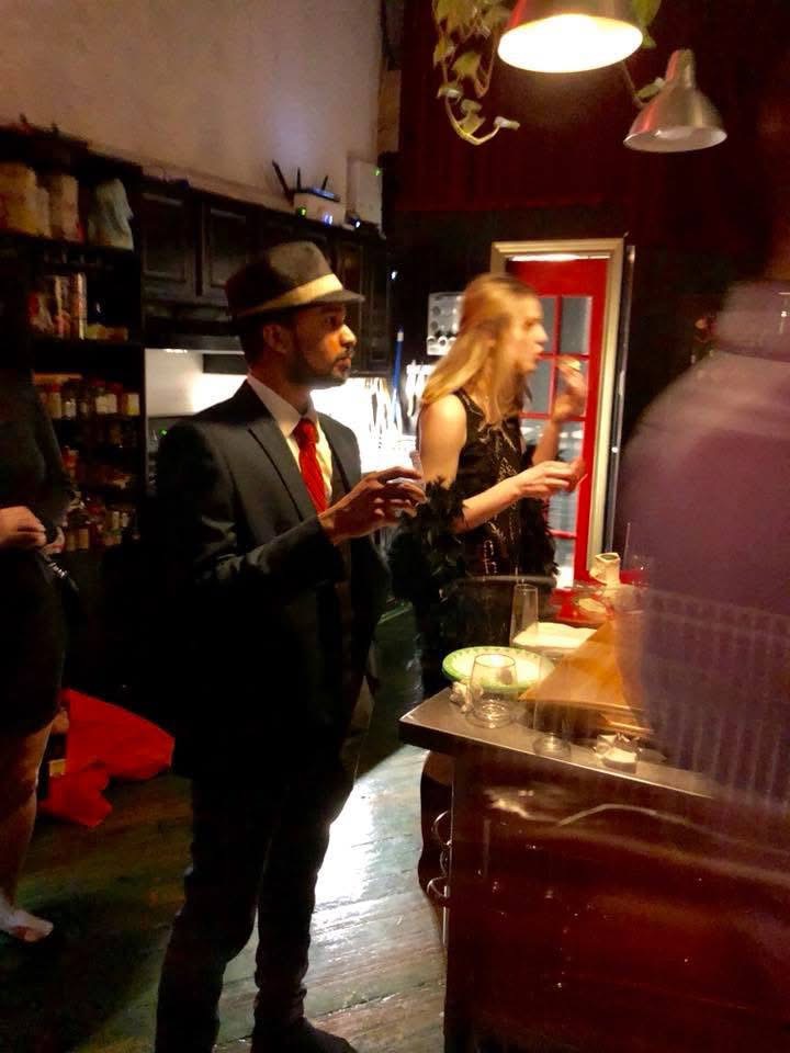 Man in 1920s suit and fedora holding a cocktail at a speakeasy bar with warm amber lighting — Prohibition-era throwback