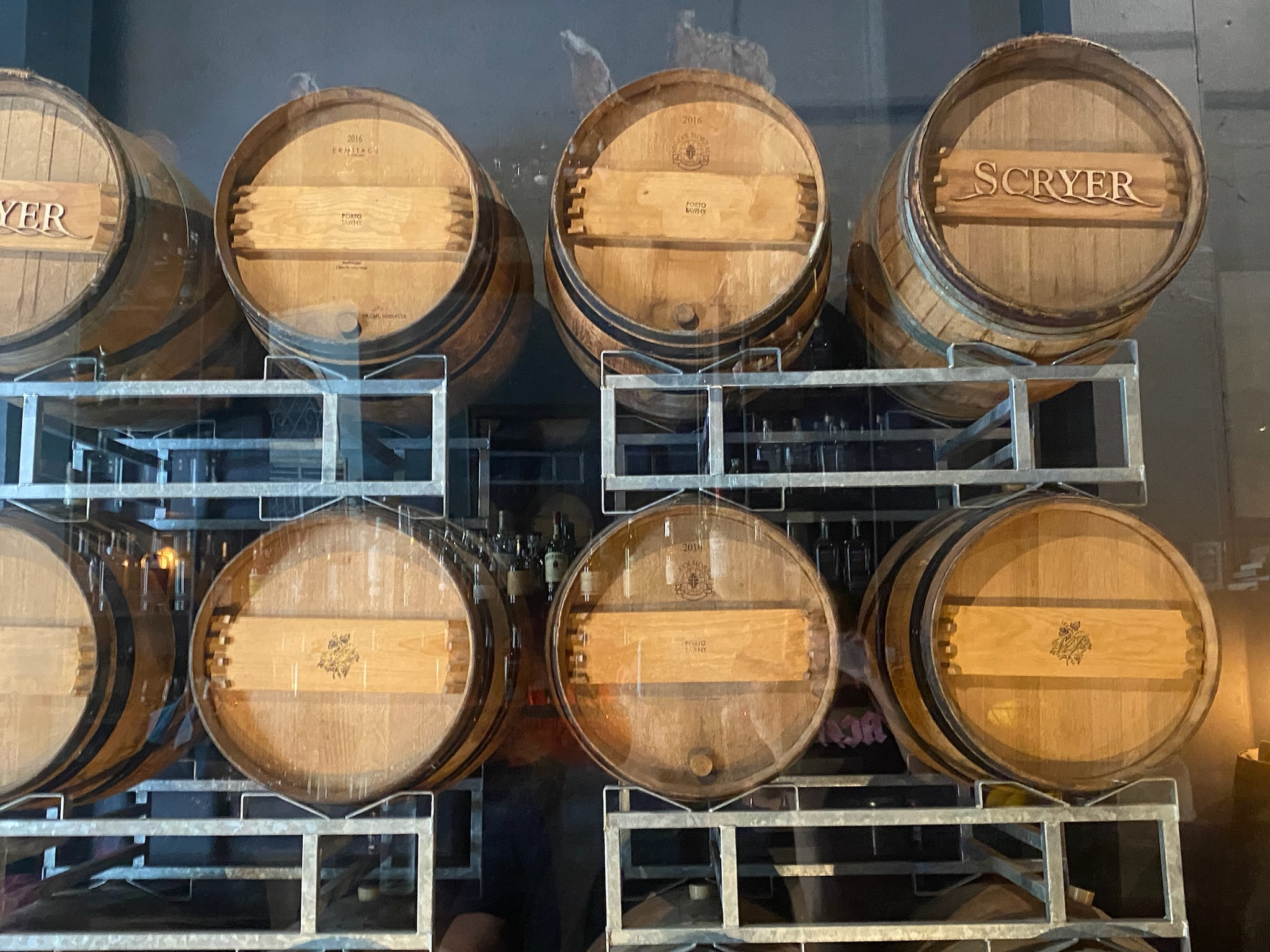Scryer Rum aging barrels \u2014 rows of oak wine-seasoned barrels stacked on metal racks behind glass, 'SCRYER' branded on the barrel heads, Old San Juan Barrelhouse
