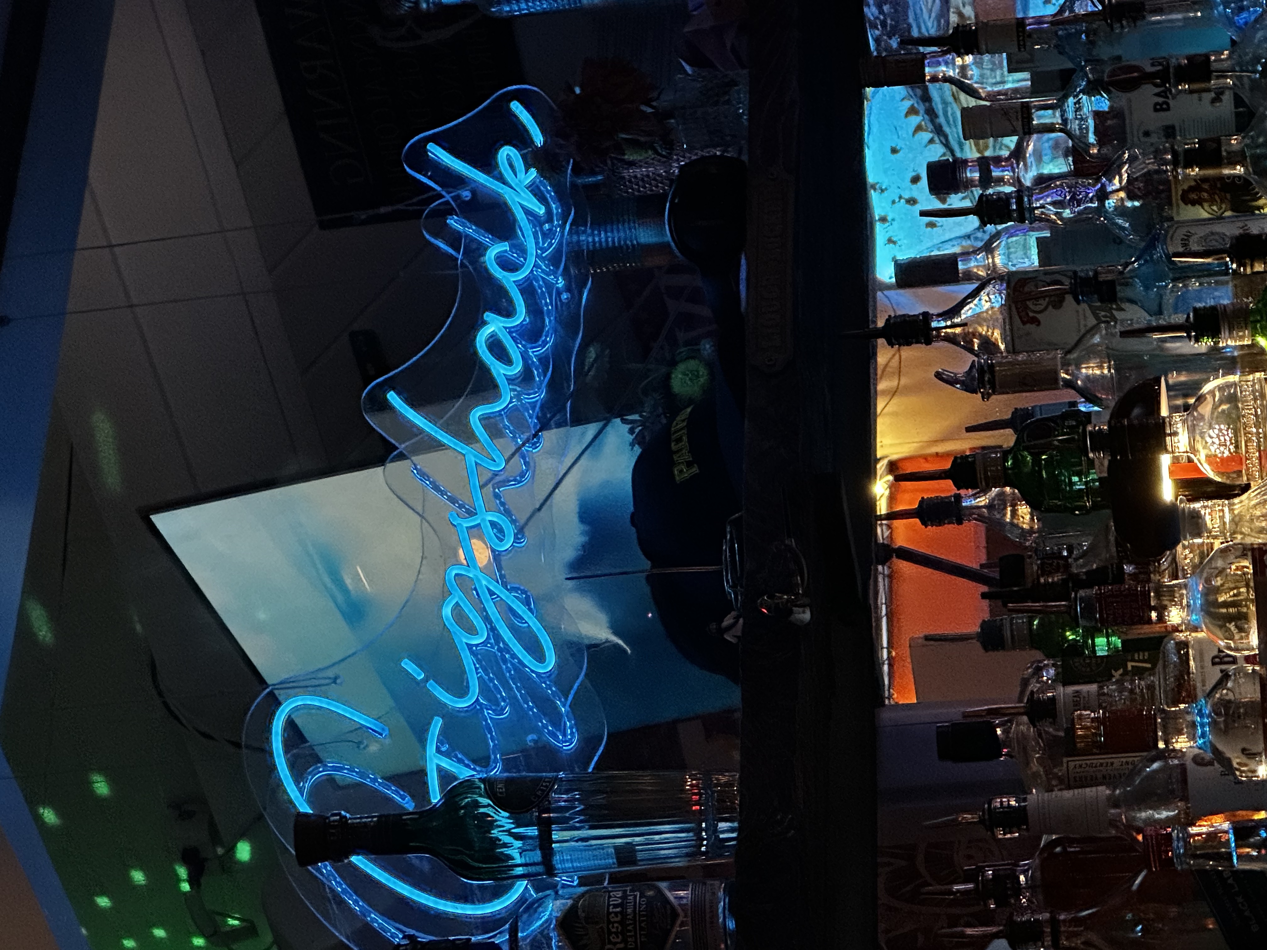 Gigshack neon sign glowing blue above the bar with bottles and spirits — 668 The Gig Shack, Montauk