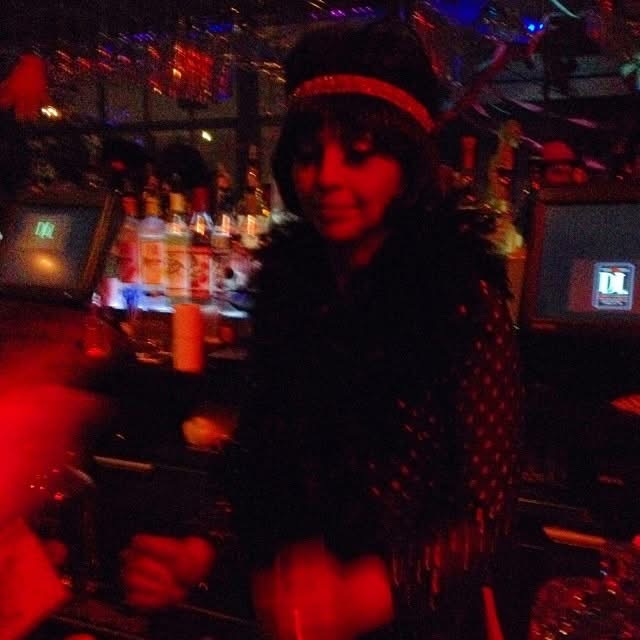 Woman in 1920s-inspired dark outfit with hat at a dimly lit bar with red and blue lighting β Prohibition-era Halloween party throwback