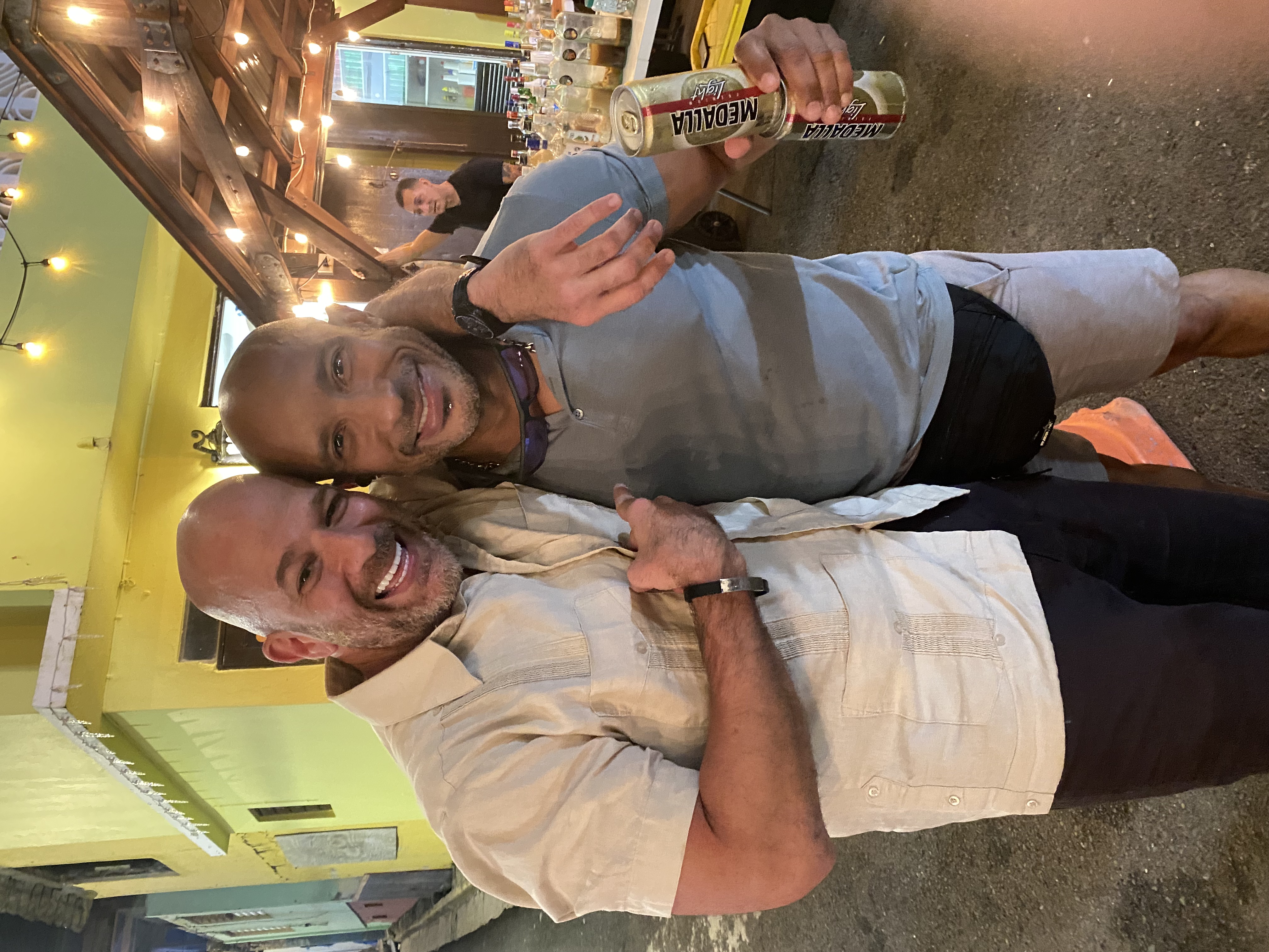 Xavier with a friend at an outdoor bar in Old San Juan — string lights, Medalla beer
