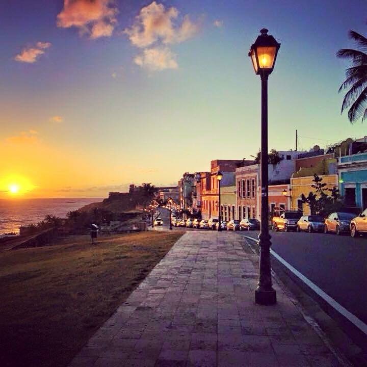 Sunset along the waterfront promenade in Old San Juan β street lamp glowing, colorful buildings, ocean horizon