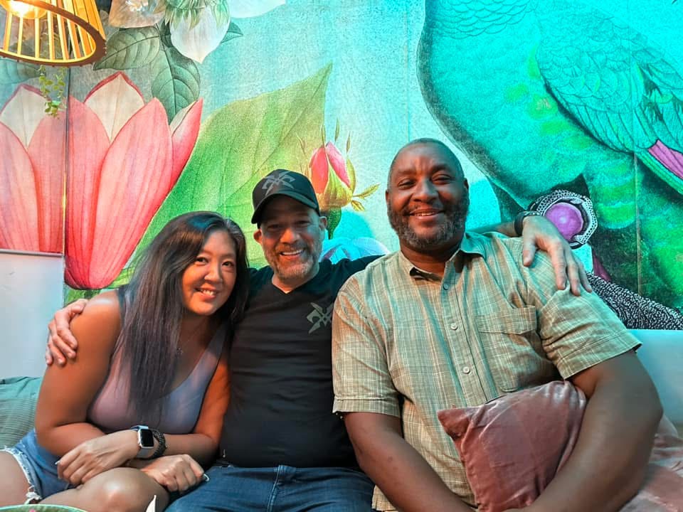 Three friends relaxing at a lounge with a vibrant floral mural backdrop in Puerto Rico