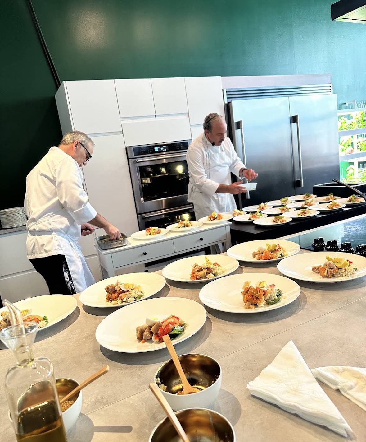 Two chefs plating dishes at Epicuro — white chef coats, rows of beautifully plated dishes with colorful garnishes