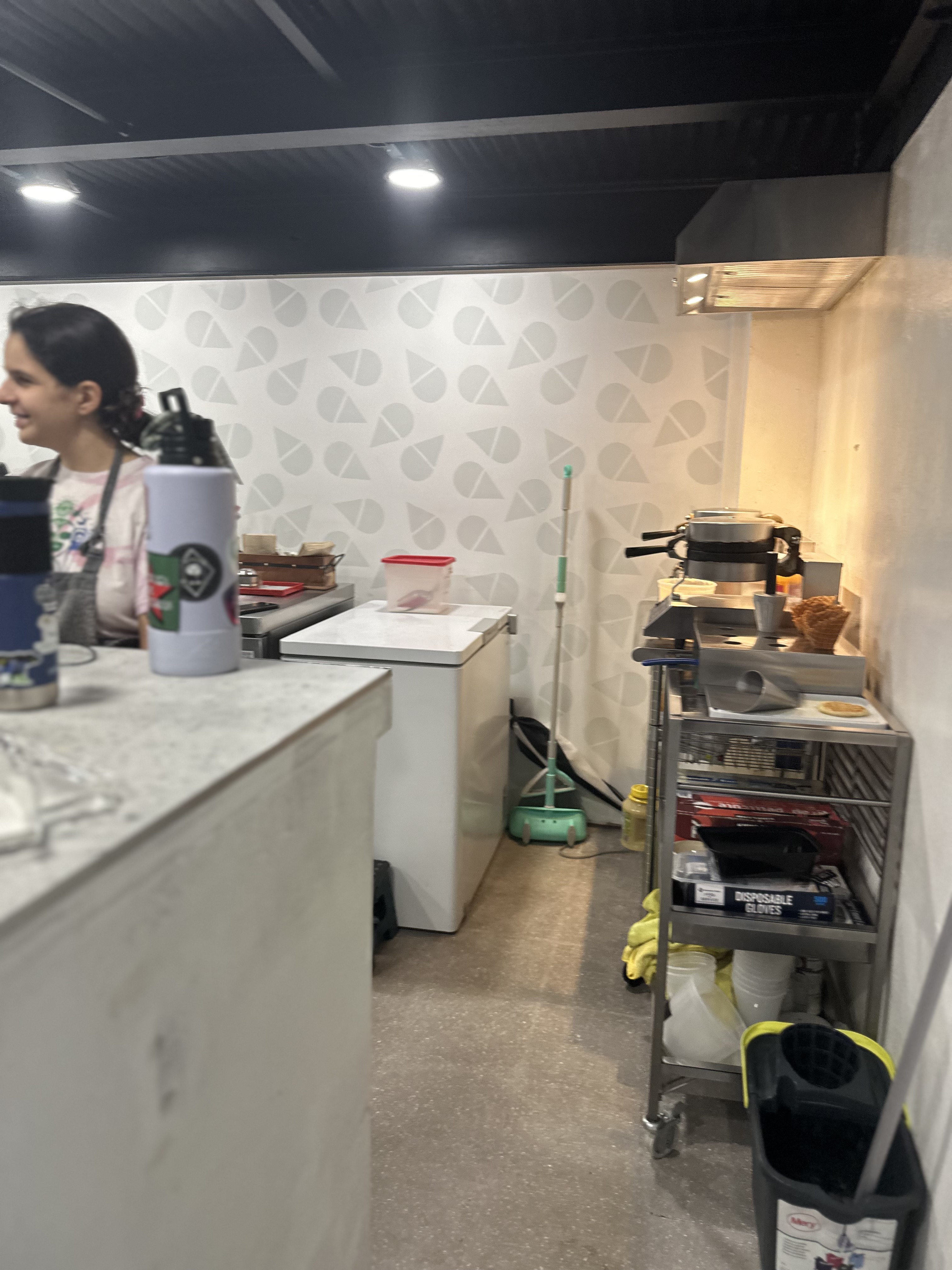 Via Lactea ice cream shop interior — behind the counter with freezer, waffle cone maker, and a worker scooping ice cream — hidden behind the MO hair salon in Santurce