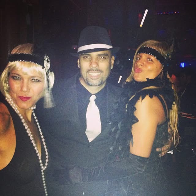 Man in 1920s suit and fedora with two women in flapper headbands, pearls, and feather boas β Halloween Prohibition party throwback