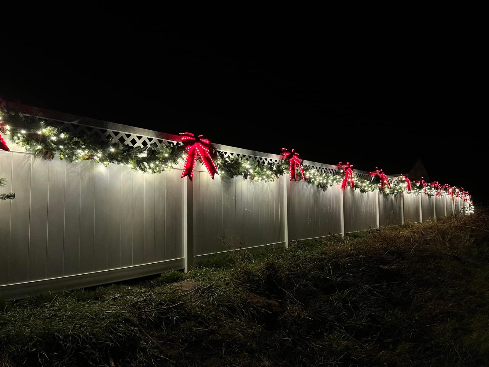 Fence line decorated with lit garland and red bows — professional Christmas light installation in Nebraska