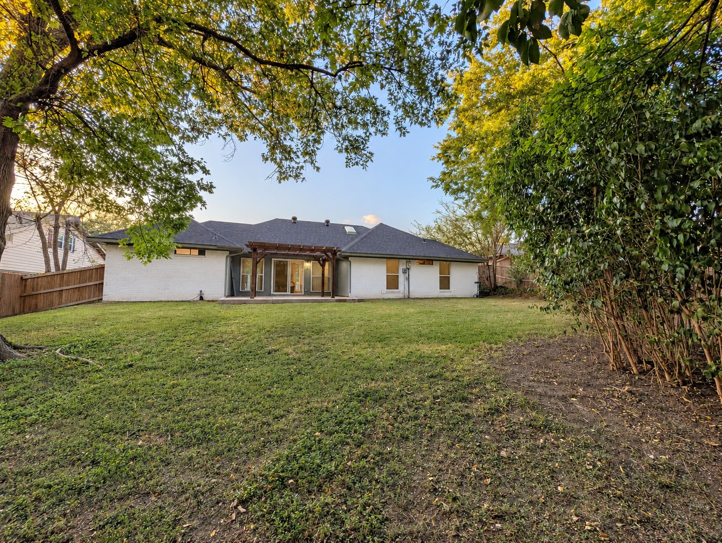Fenced backyard with mature trees and pergola-covered patio
