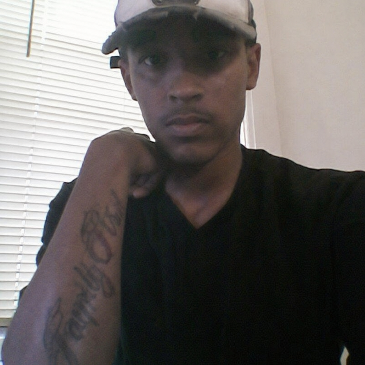 Javon in a brighter portrait photo wearing a cap, showing his forearm tattoo
