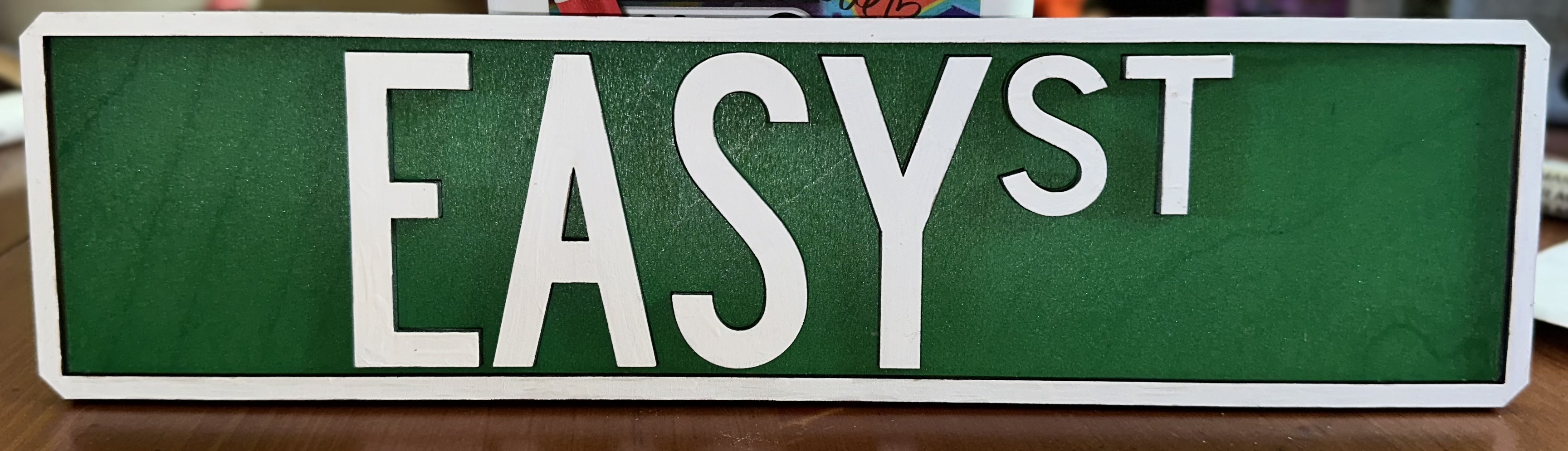 Green laser-cut EASY ST street sign with white painted lettering on a wooden surface