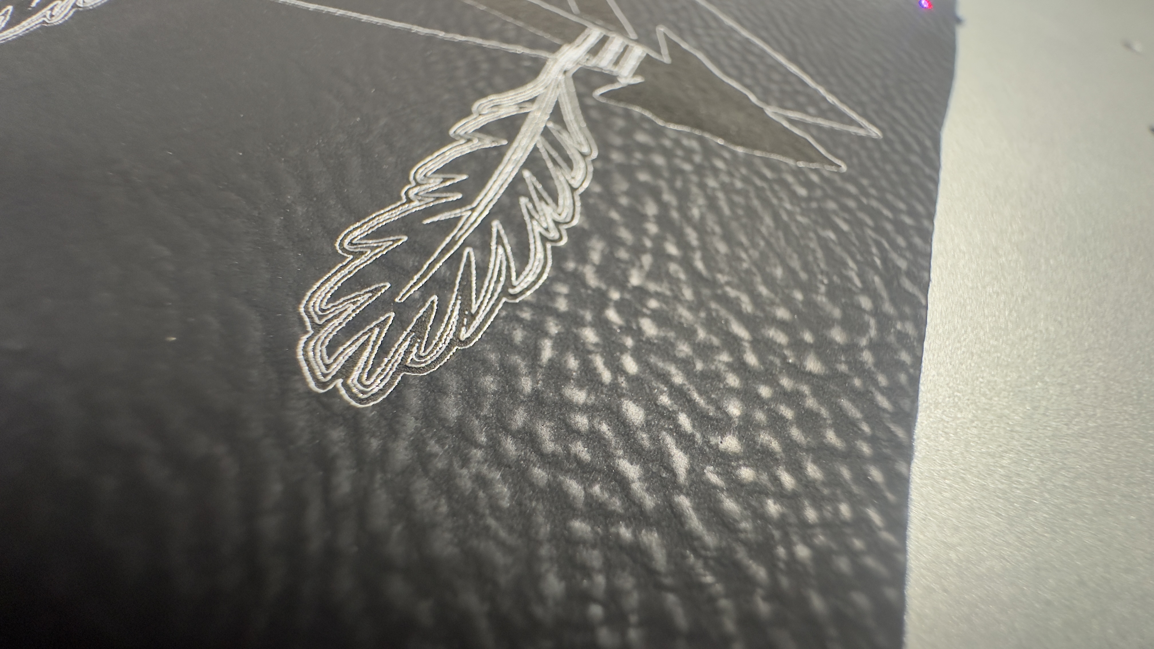 Close-up of laser-engraved feather detail on black leather