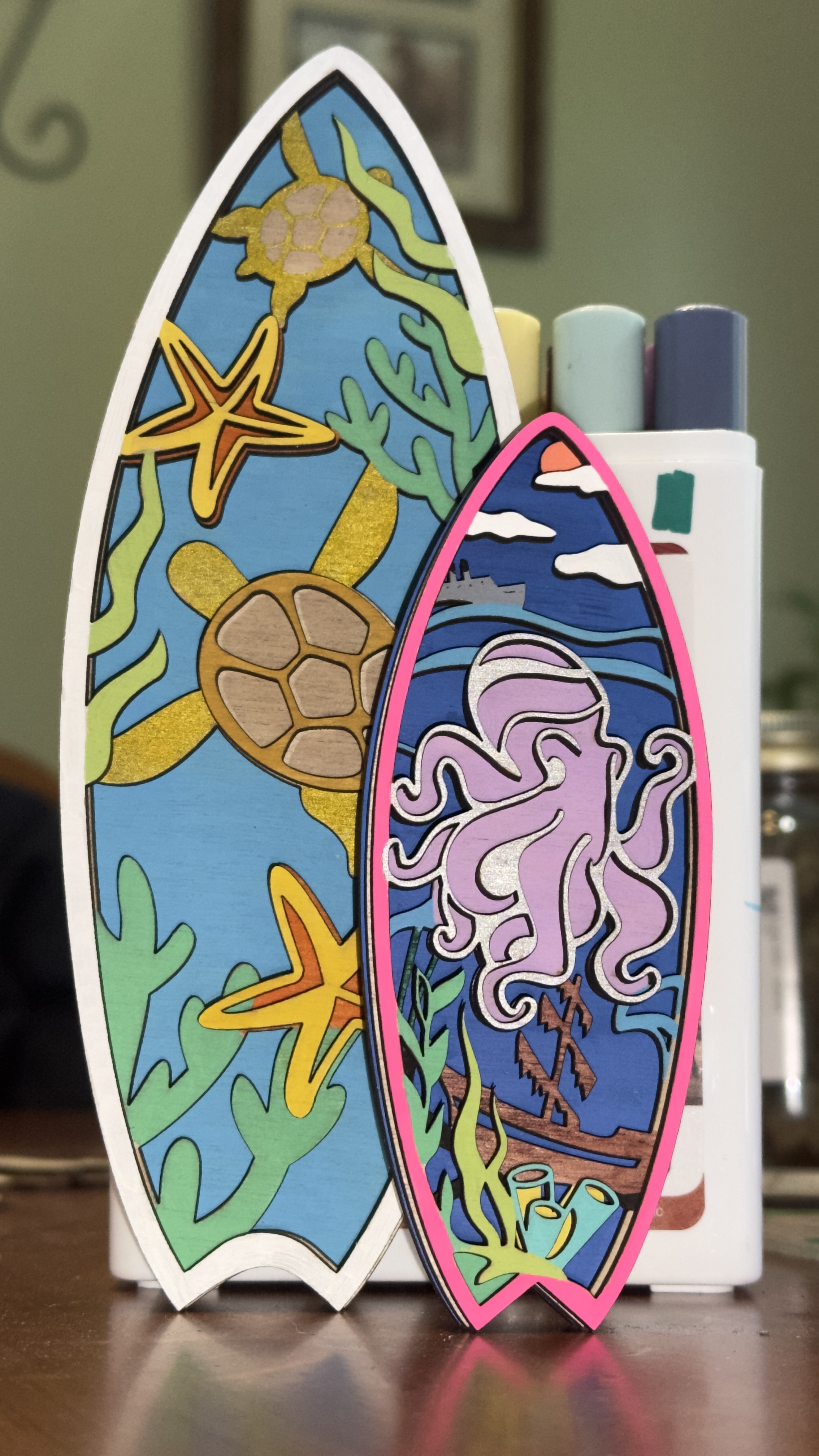 Layered laser-cut wooden surfboard art pieces with colorful ocean scenes featuring sea turtles, starfish, octopus, and seaweed