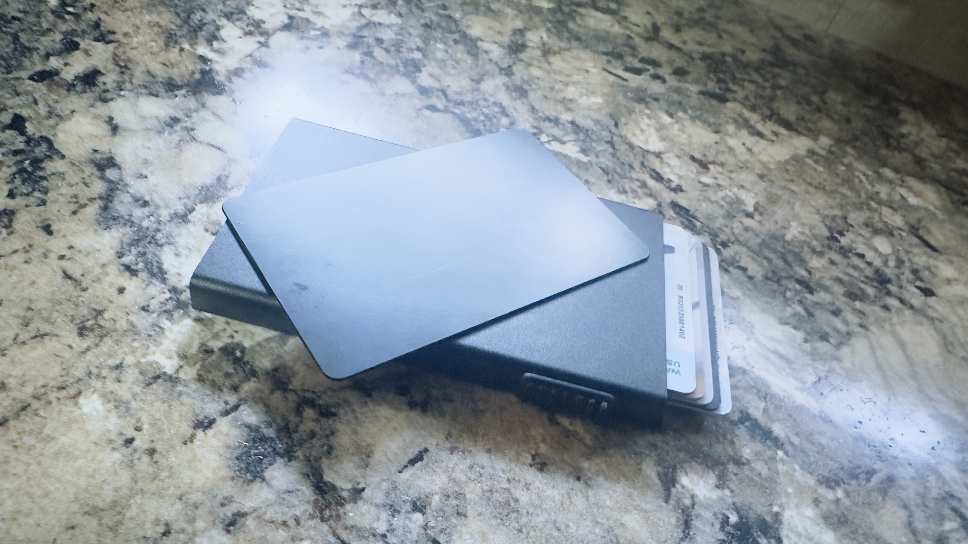 NFC-enabled laser-cut metal business cards with brushed finish and programmable NFC tag in a slim card holder on granite countertop