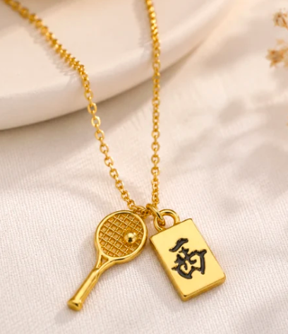 Gold necklace with a tennis racket charm and a gold Mahjong tile pendant on a delicate chain
