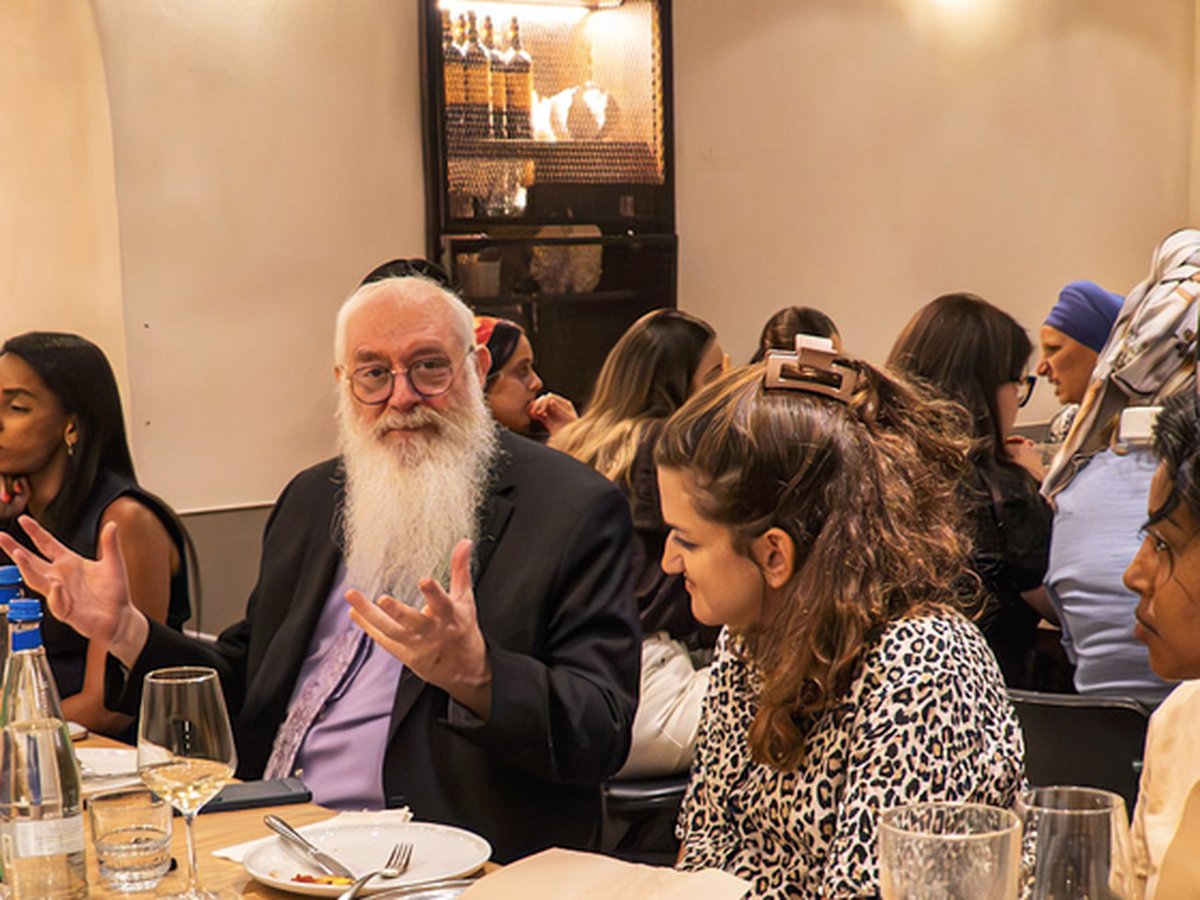 Rabbi Mentz speaking with the widows at dinner, gesturing with his hands