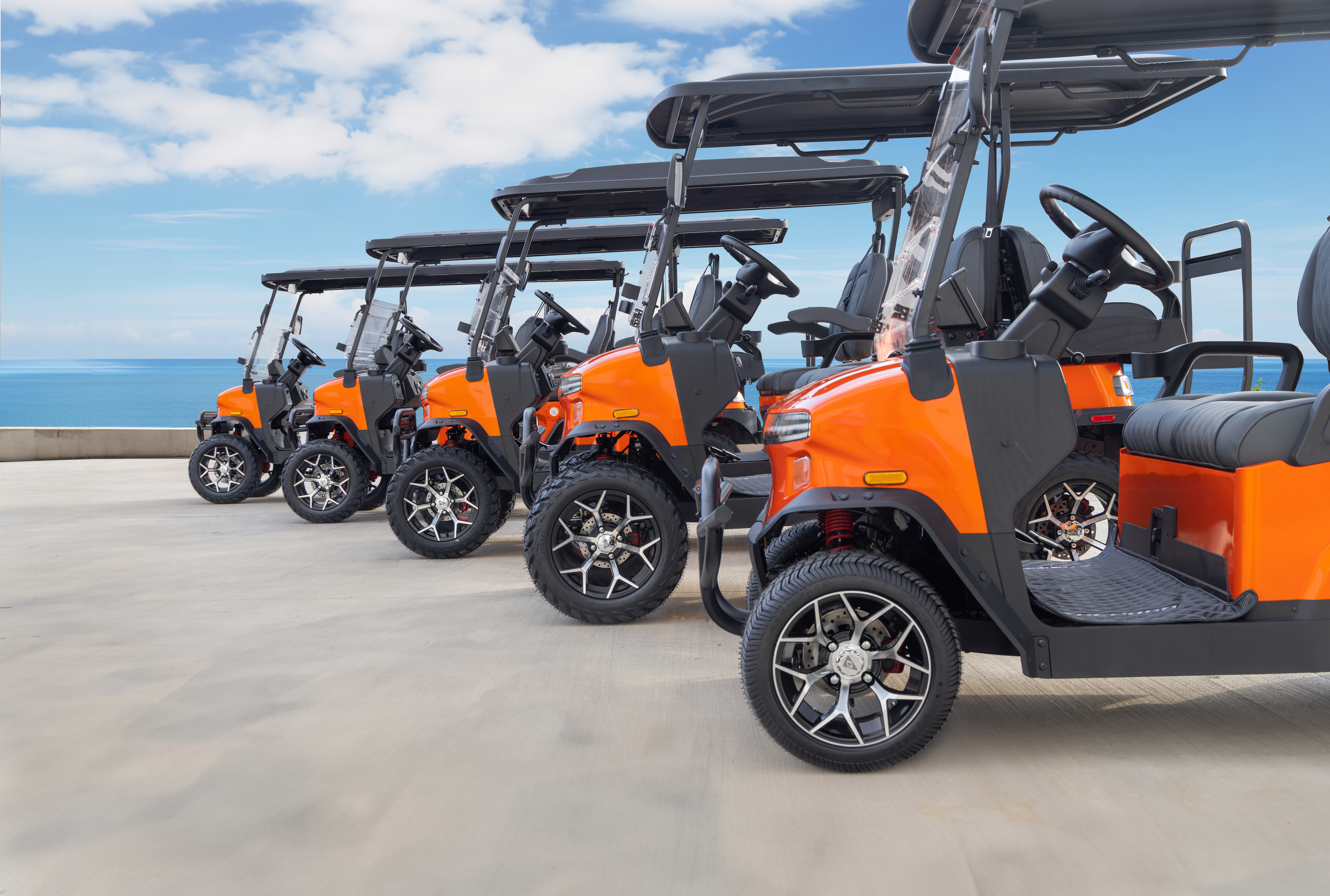 Row of orange Denago EV golf carts lined up at a coastal location