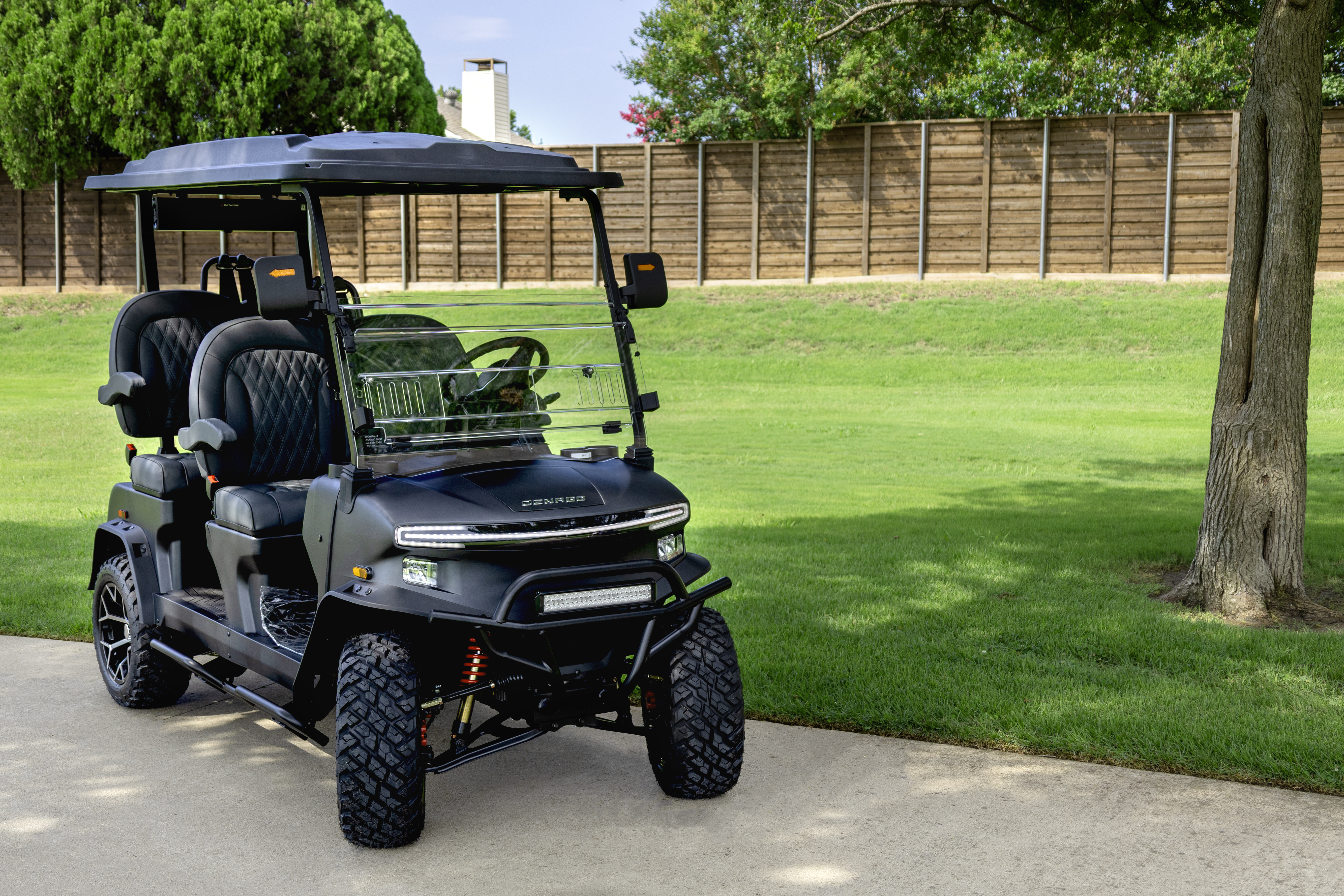 Black Denago EV golf cart with LED light bar and aggressive off-road tires on a driveway