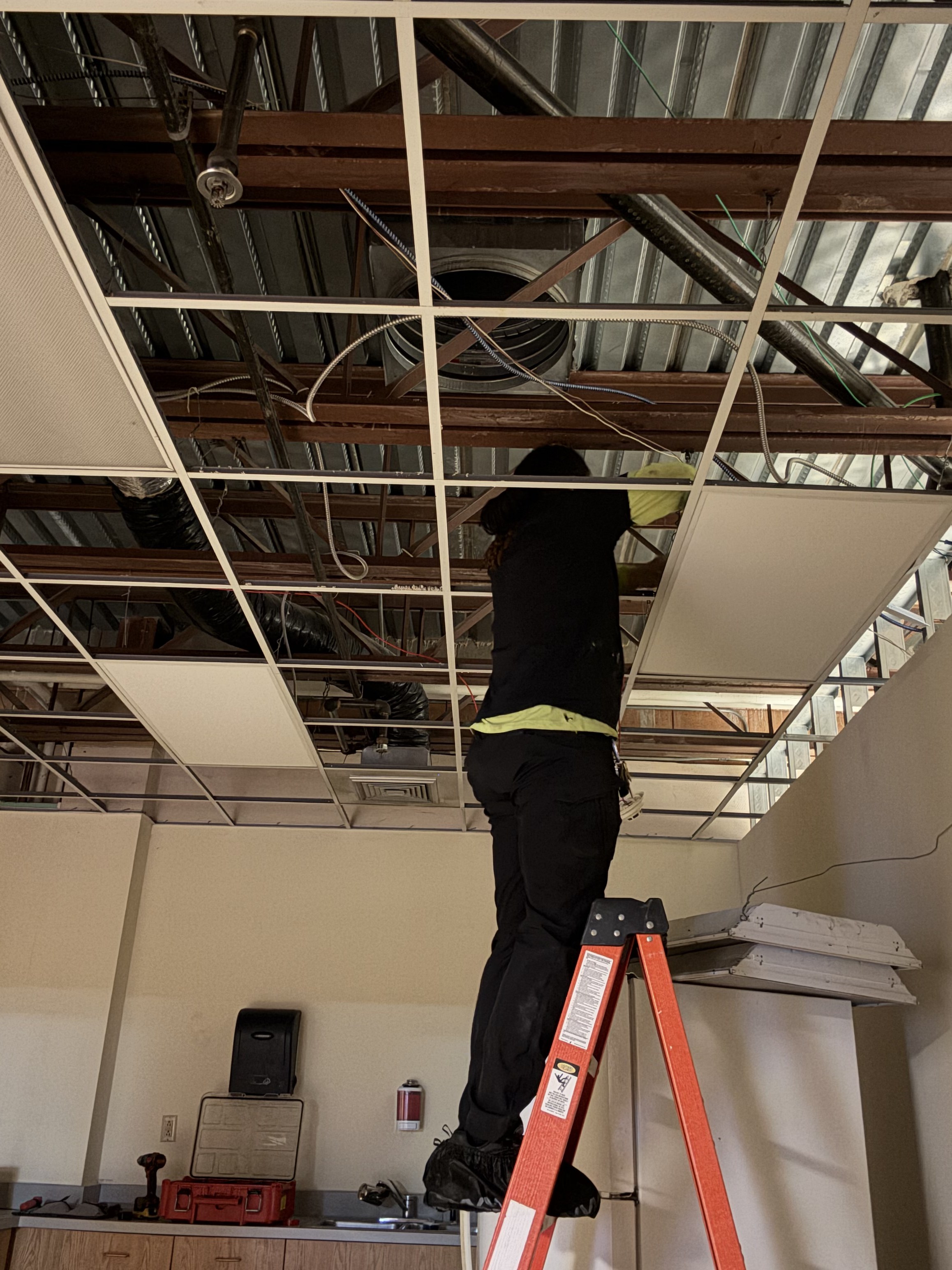 Electrician working in commercial drop ceiling grid running wiring during commercial electrical project โ Rochester NY