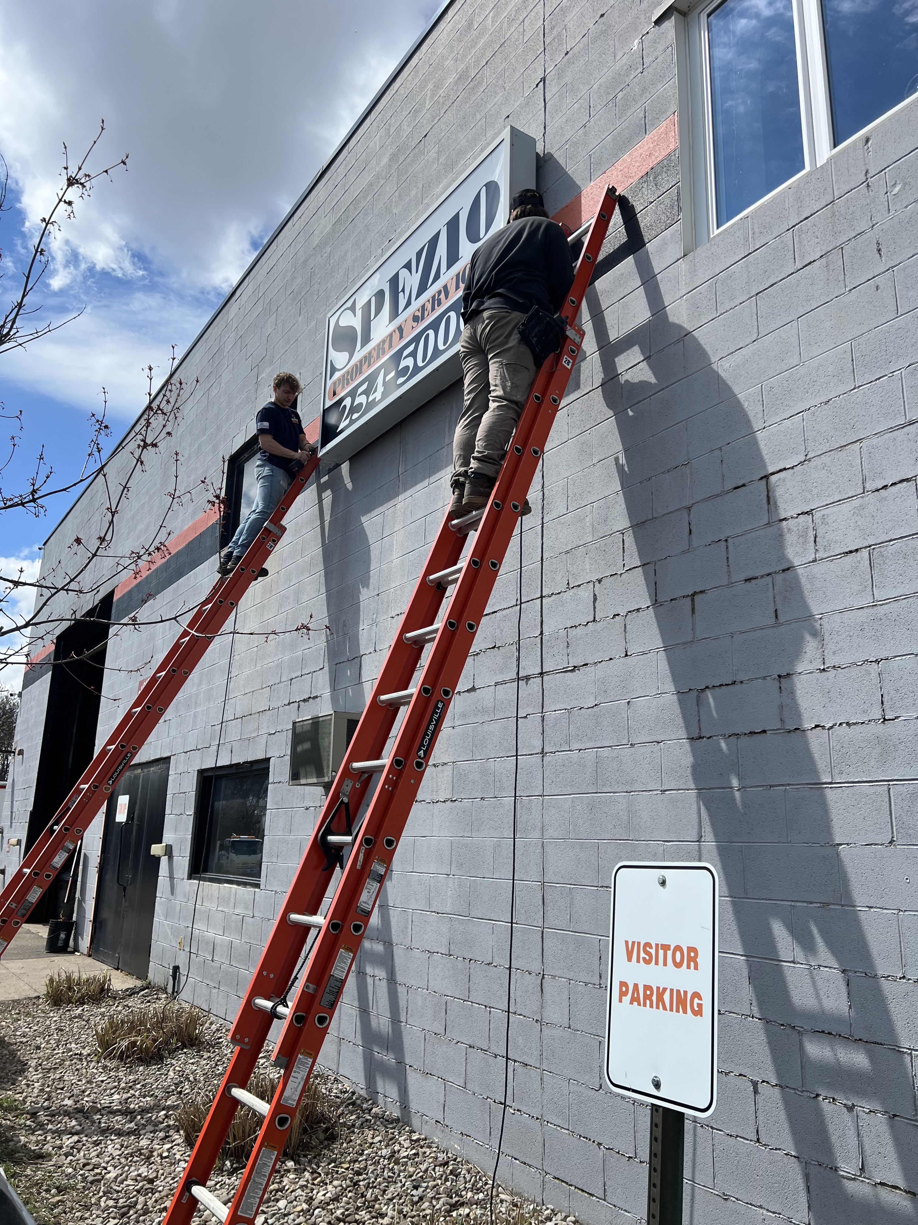Two Premier Alarms and Electric crew members on extension ladders doing exterior commercial electrical work โ Rochester NY
