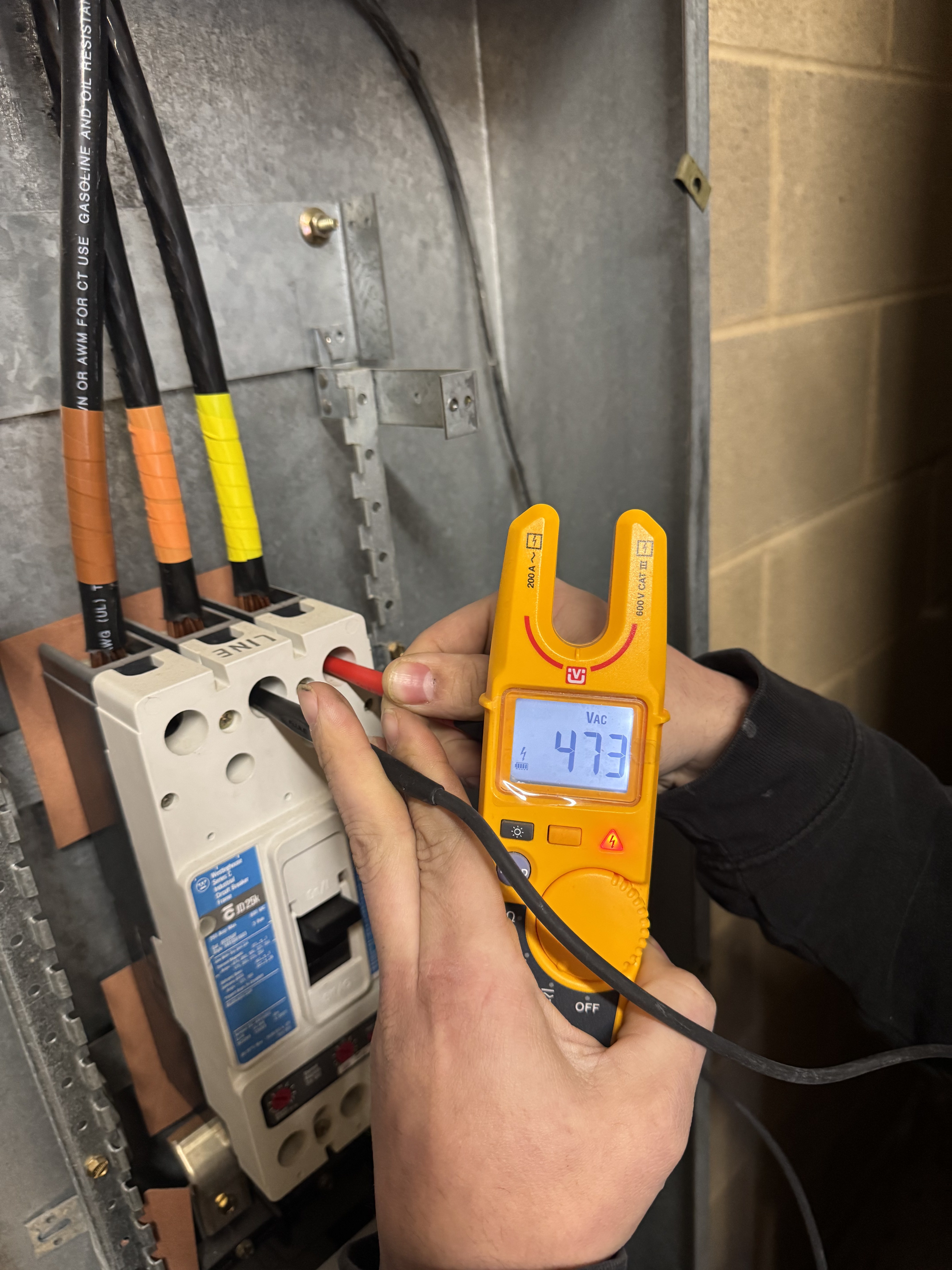 Licensed electrician using Fluke clamp meter testing 473V on commercial electrical panel during emergency service call โ Monroe County NY